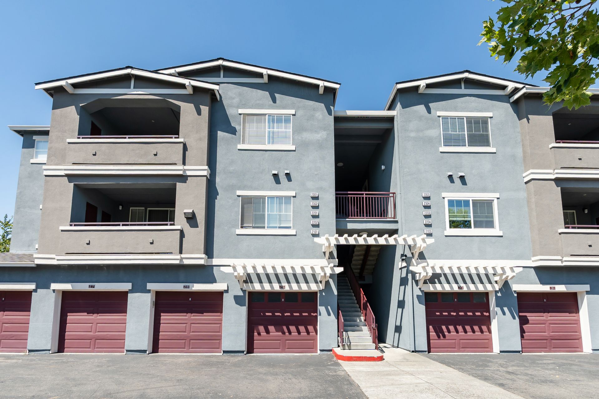 Exterior view of apartment building with private garages, covered balconies, and landscaped community grounds.