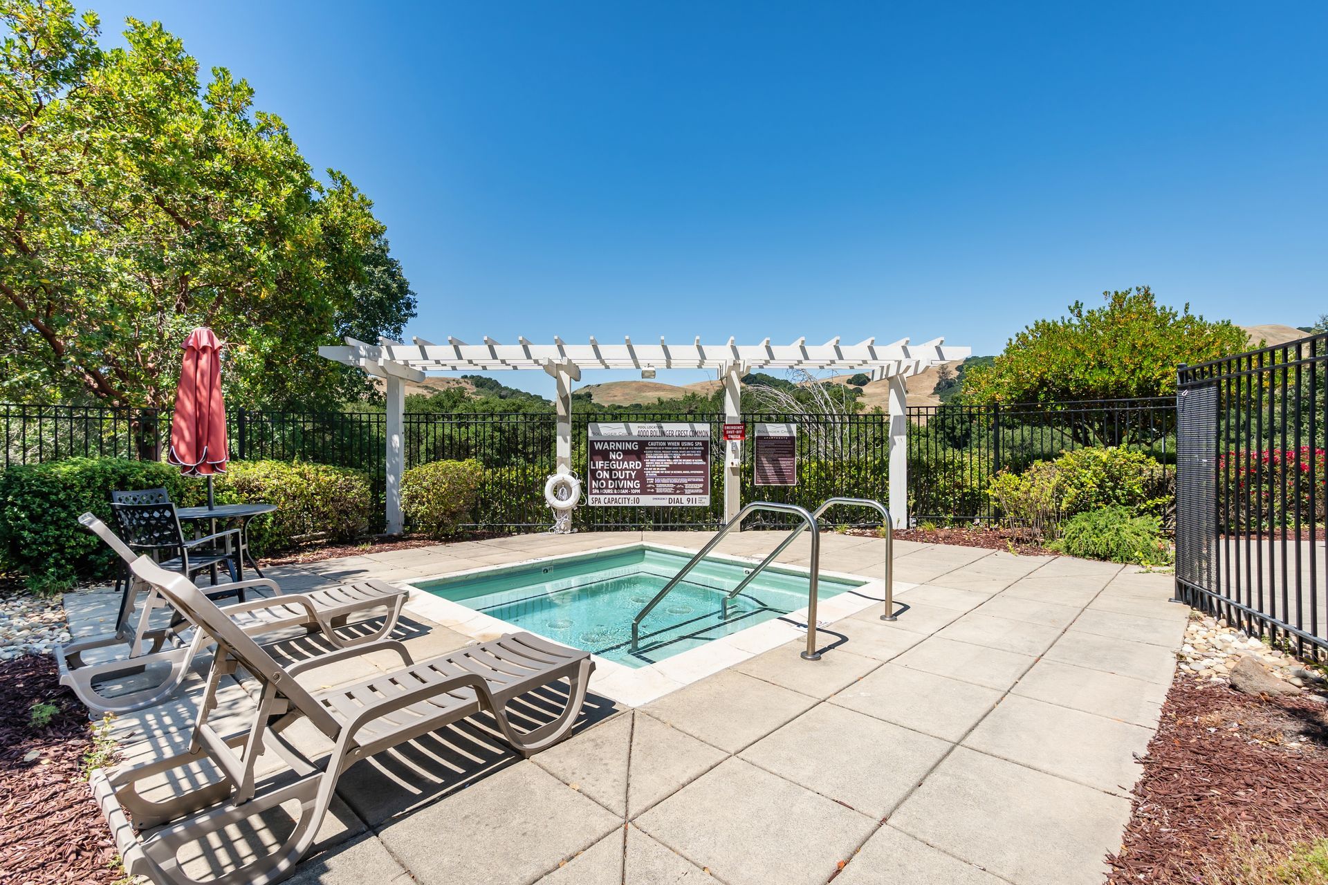 Outdoor spa with lounge chairs, shaded pergola, landscaped patio, and scenic hillside views.