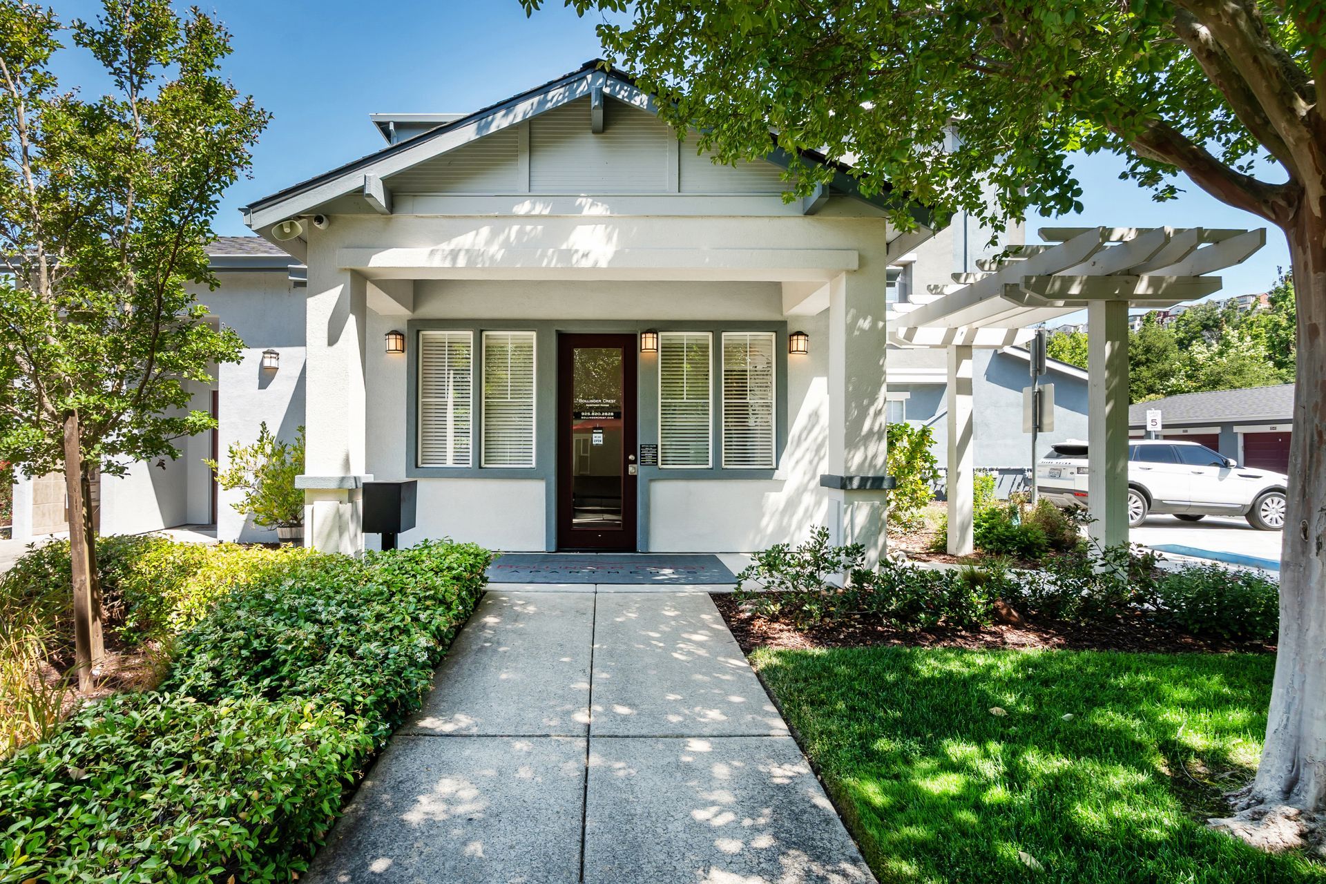 Leasing office entrance with landscaped walkways, mature trees, and a shaded pergola.