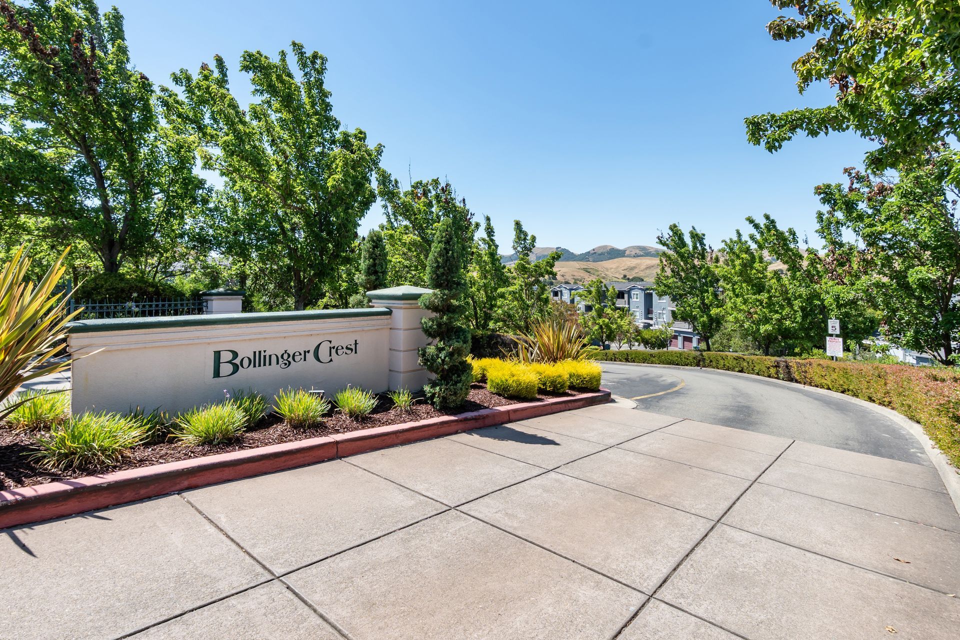 Community entrance monument sign with landscaped grounds, mature trees, and scenic hillside views.