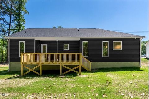 Single-story black house with a wooden front deck and porch railing on a grassy lot under a blue sky