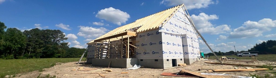 Partially built house with white siding and exposed framing under a blue sky on a rural lot