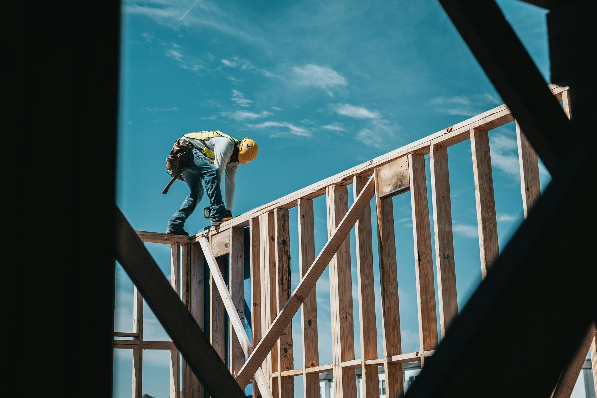 Construction worker on a wooden frame against a blue sky, viewed through a dark opening.