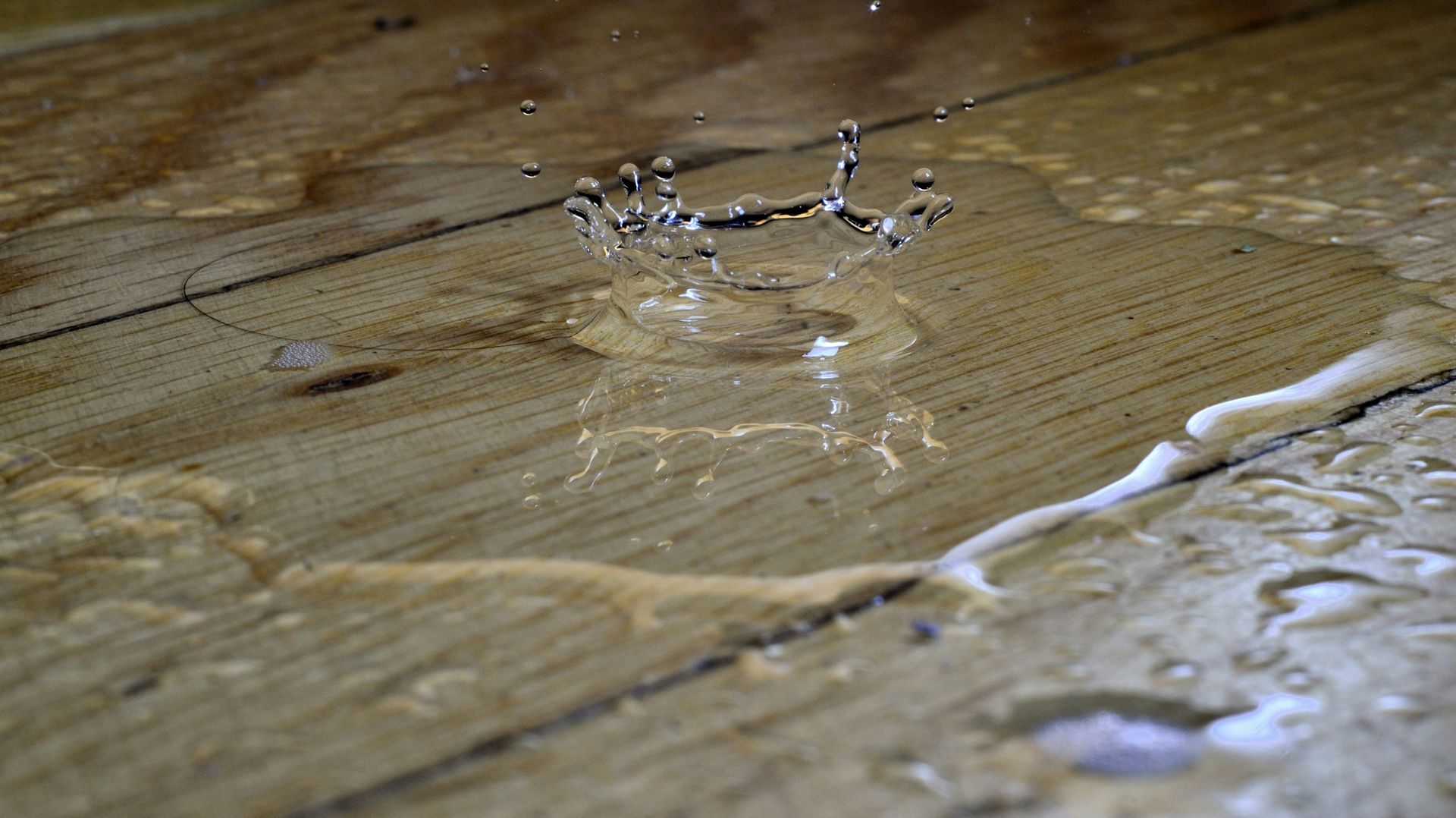 Water droplet splash on a wooden surface with a small pool of spilled liquid