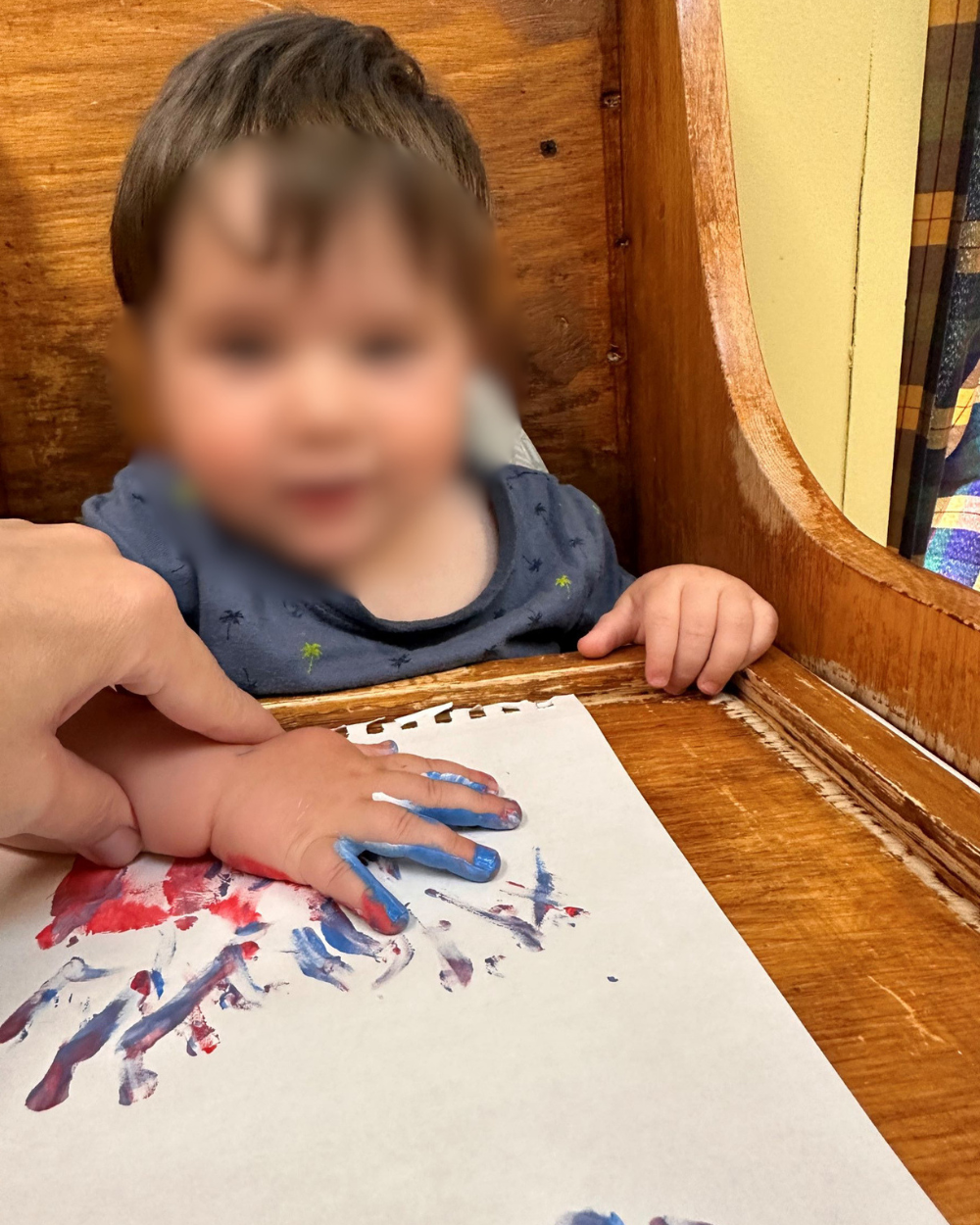 Bébé souriant lors d'une activité de peinture avec les doigts, main d'une éducatrice guidant le geste