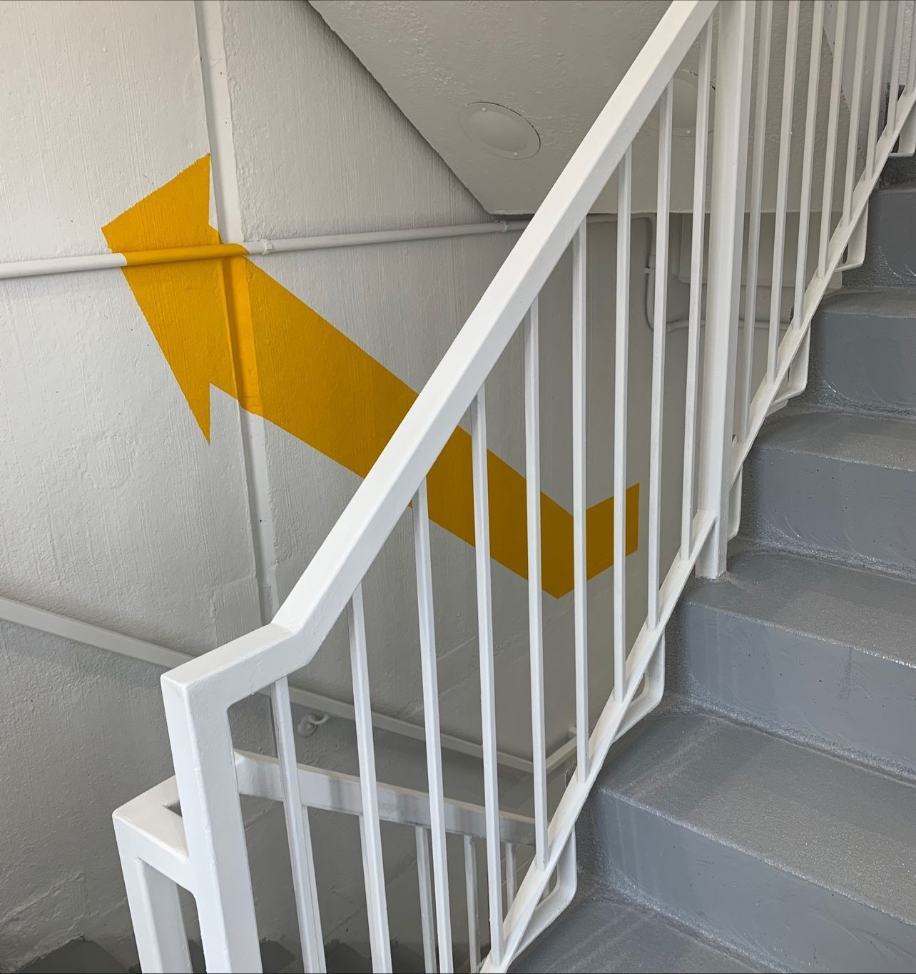 A white railing with a yellow arrow painted on the wall