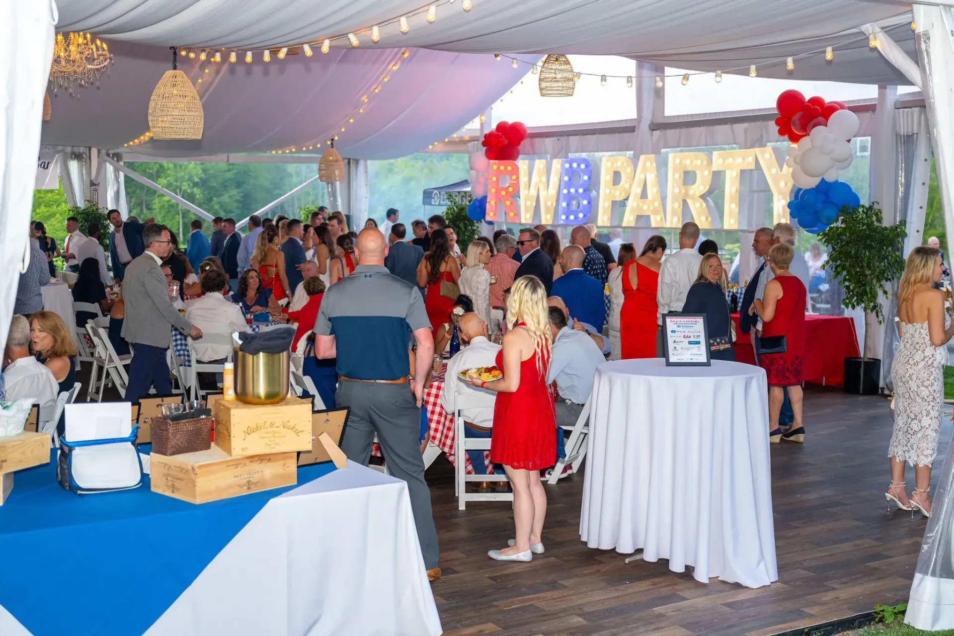 A large group of people are gathered under a tent at a party.