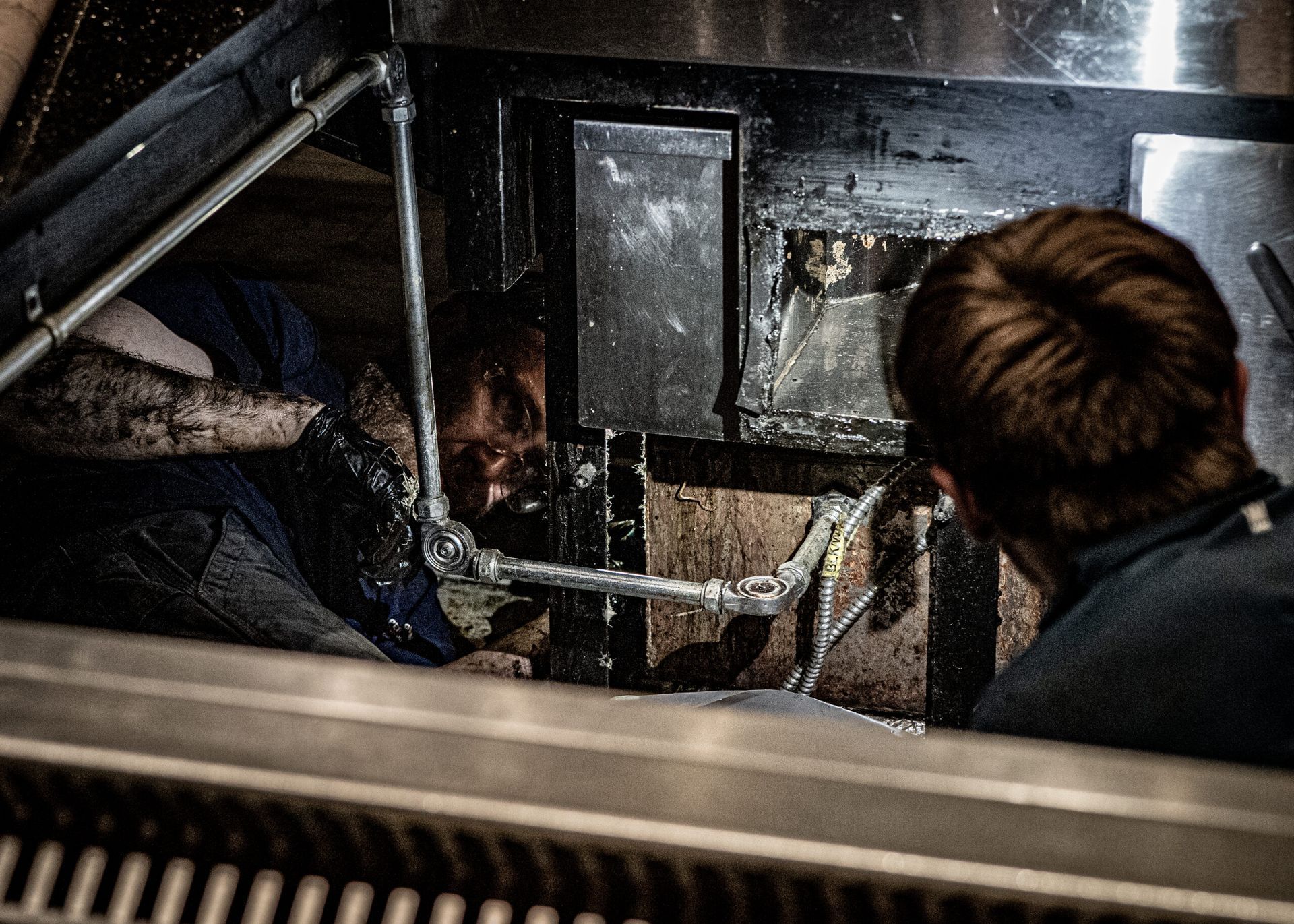 Technicians inspecting and repairing commercial kitchen exhaust system.