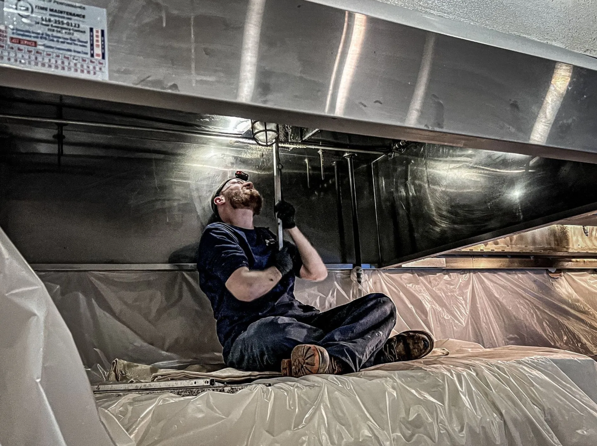 Men inspecting pipes beneath a large metal ventilation hood
