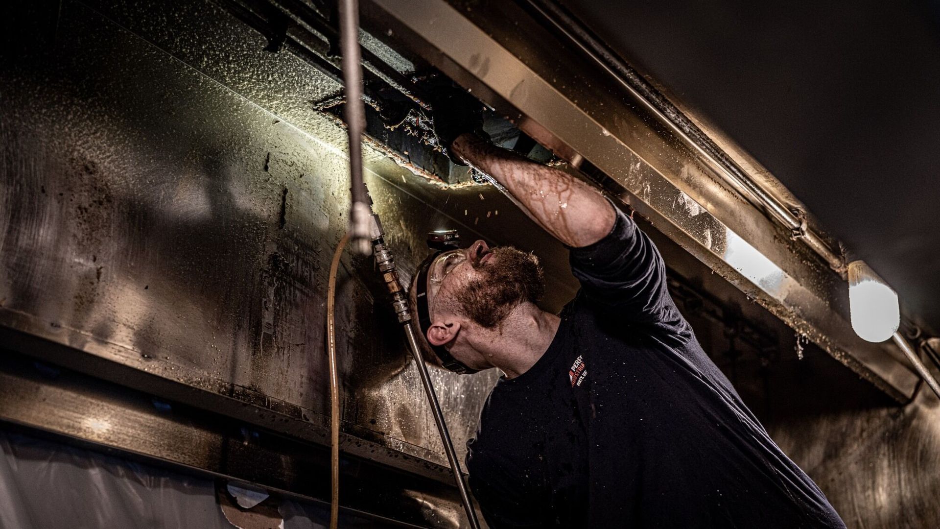 Technician cleaning grease from the interior of a commercial kitchen exhaust hood system