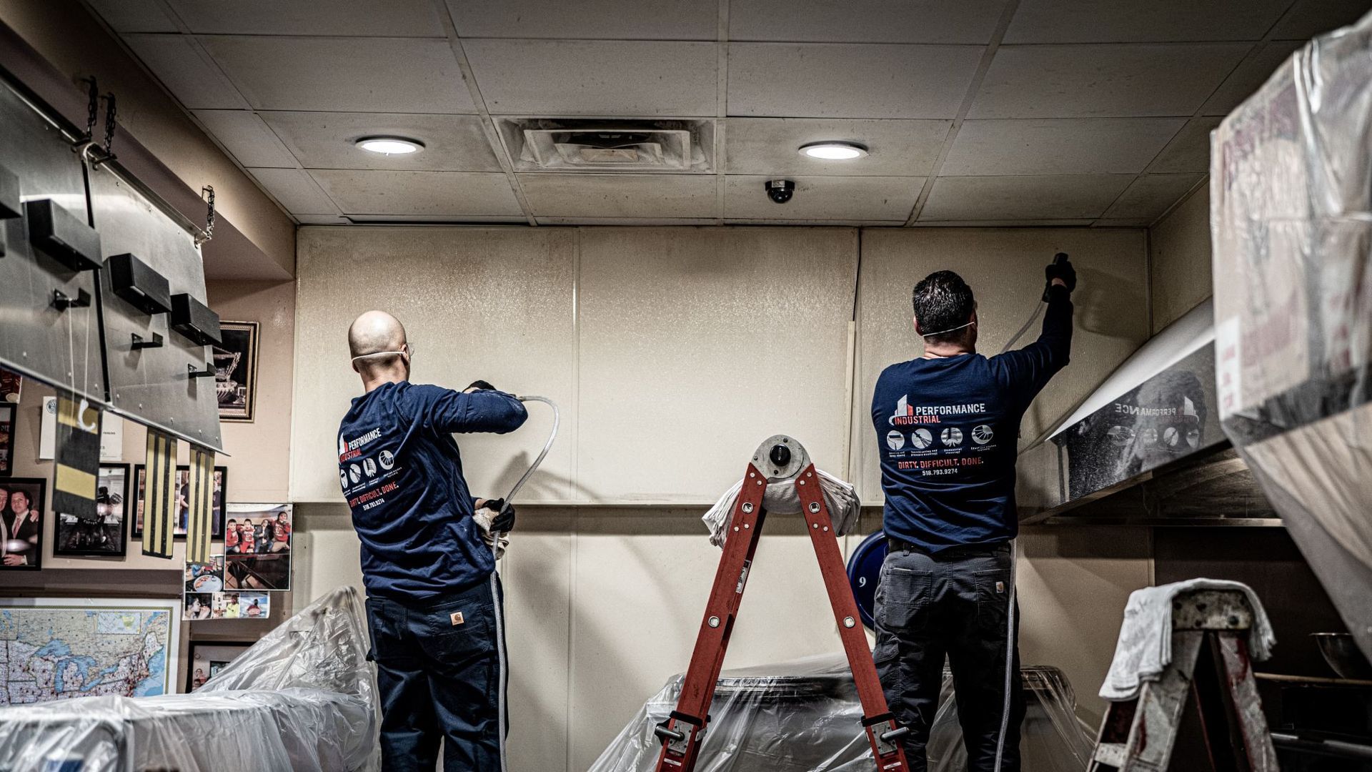Two men are working on a wall in a kitchen.