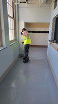 A Man In A Yellow Vest Is Standing In A Hallway Cleaning The Floor