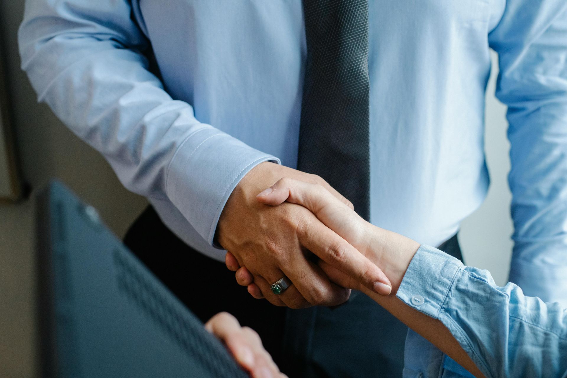 Two people shaking hands; one wearing a tie and blue shirt.