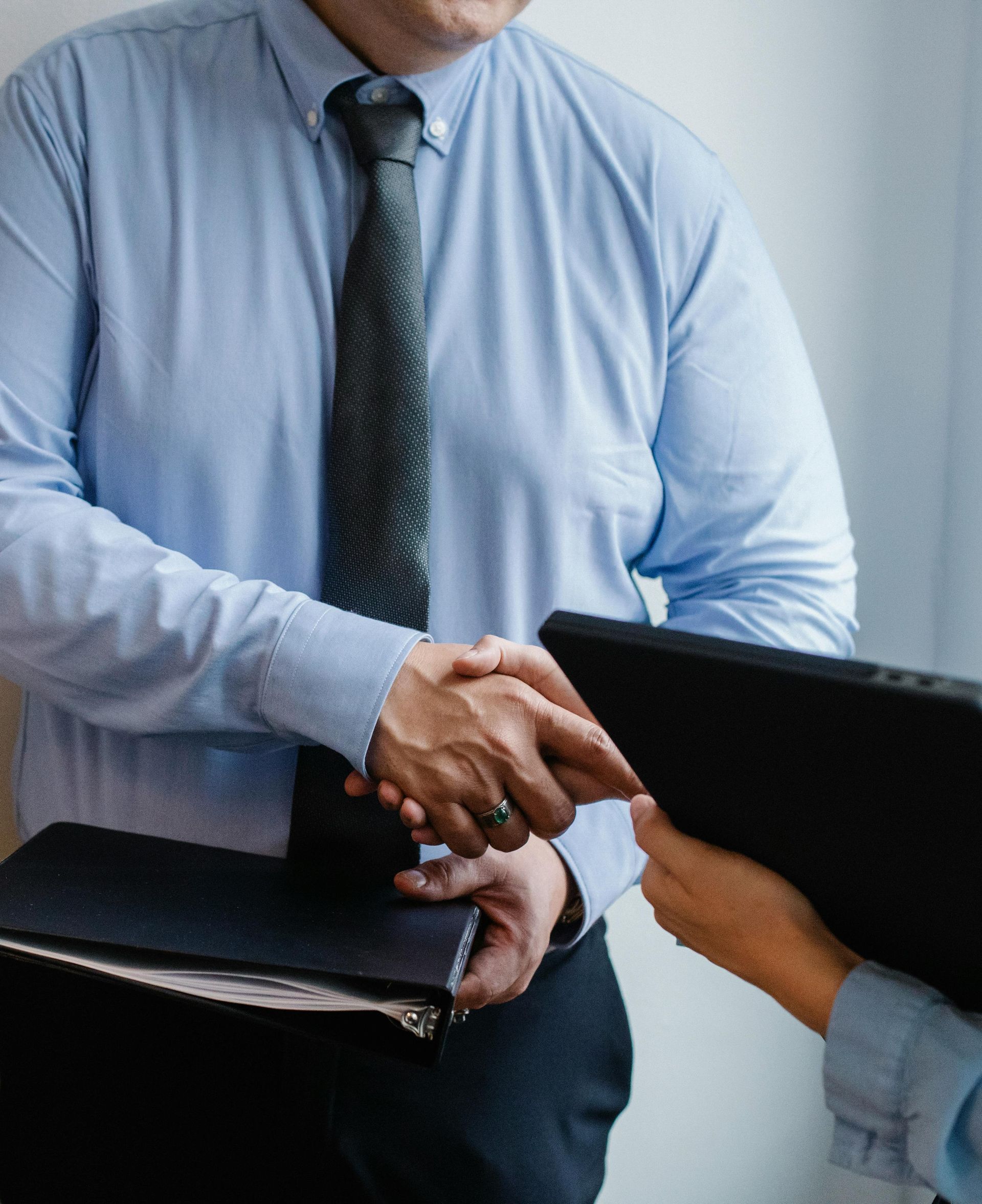 Man in blue shirt and tie shaking hands with another person, holding a briefcase.