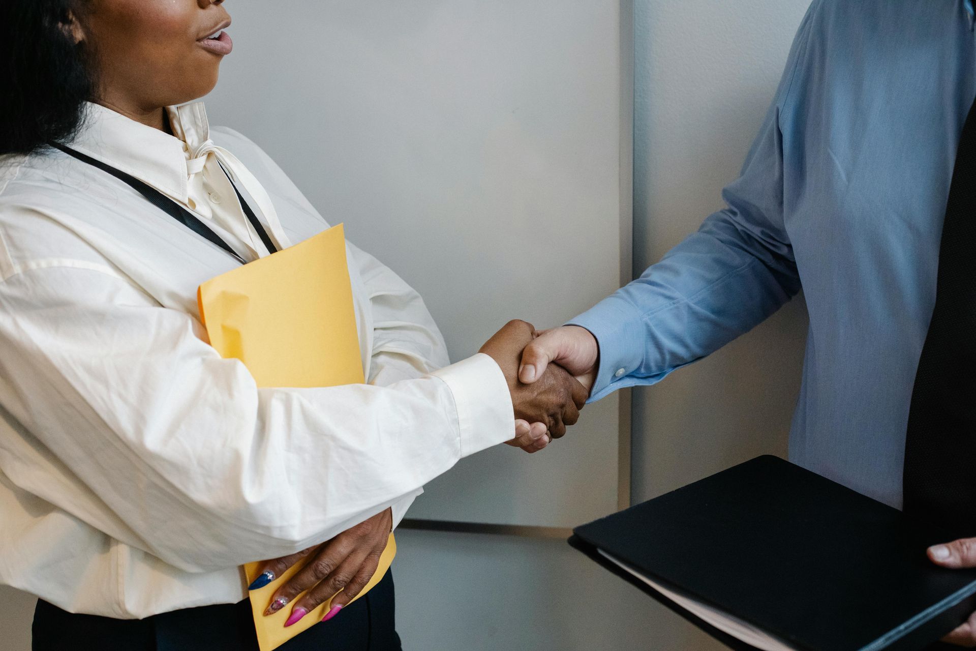 Woman in white shirt and man in blue shirt shaking hands, holding files.