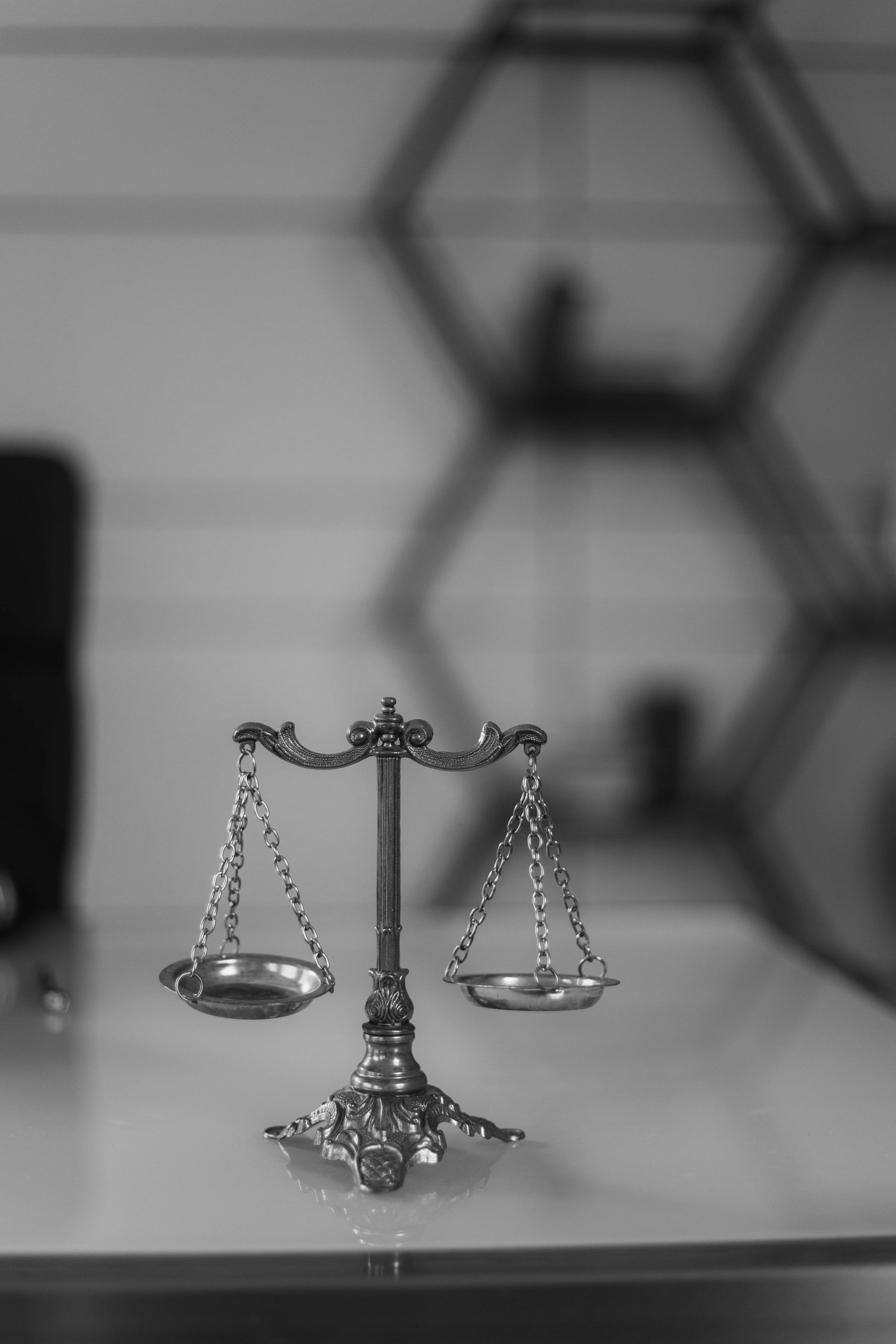 Scales of justice figurine on a reflective surface, blurred background with geometric shelving.