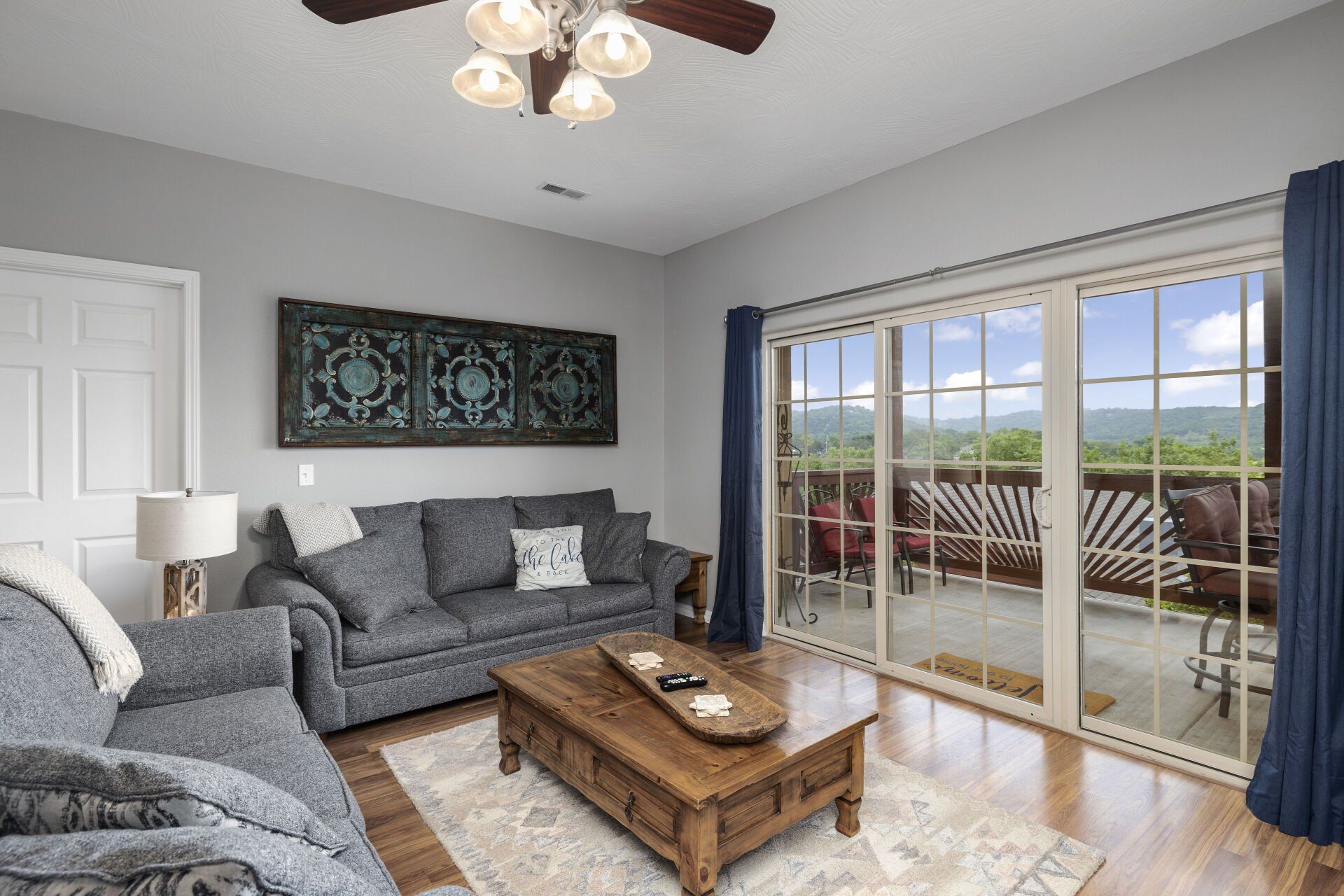 Bright living room with gray sofas, wood coffee table, wall art, and sliding glass doors to a balcony with ocean view