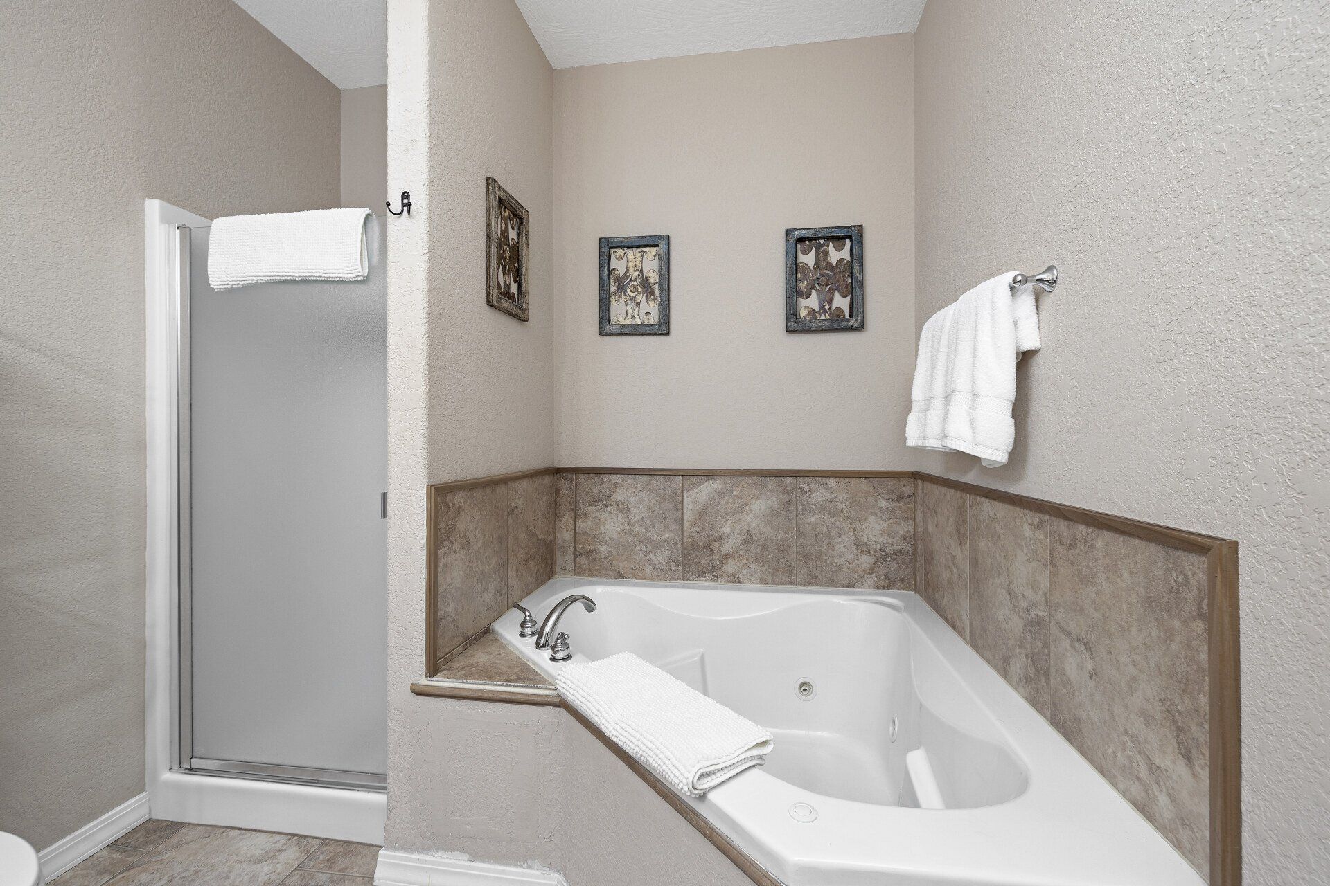 Bathroom with a white soaking tub, tiled shower, and beige walls with framed art and towels.