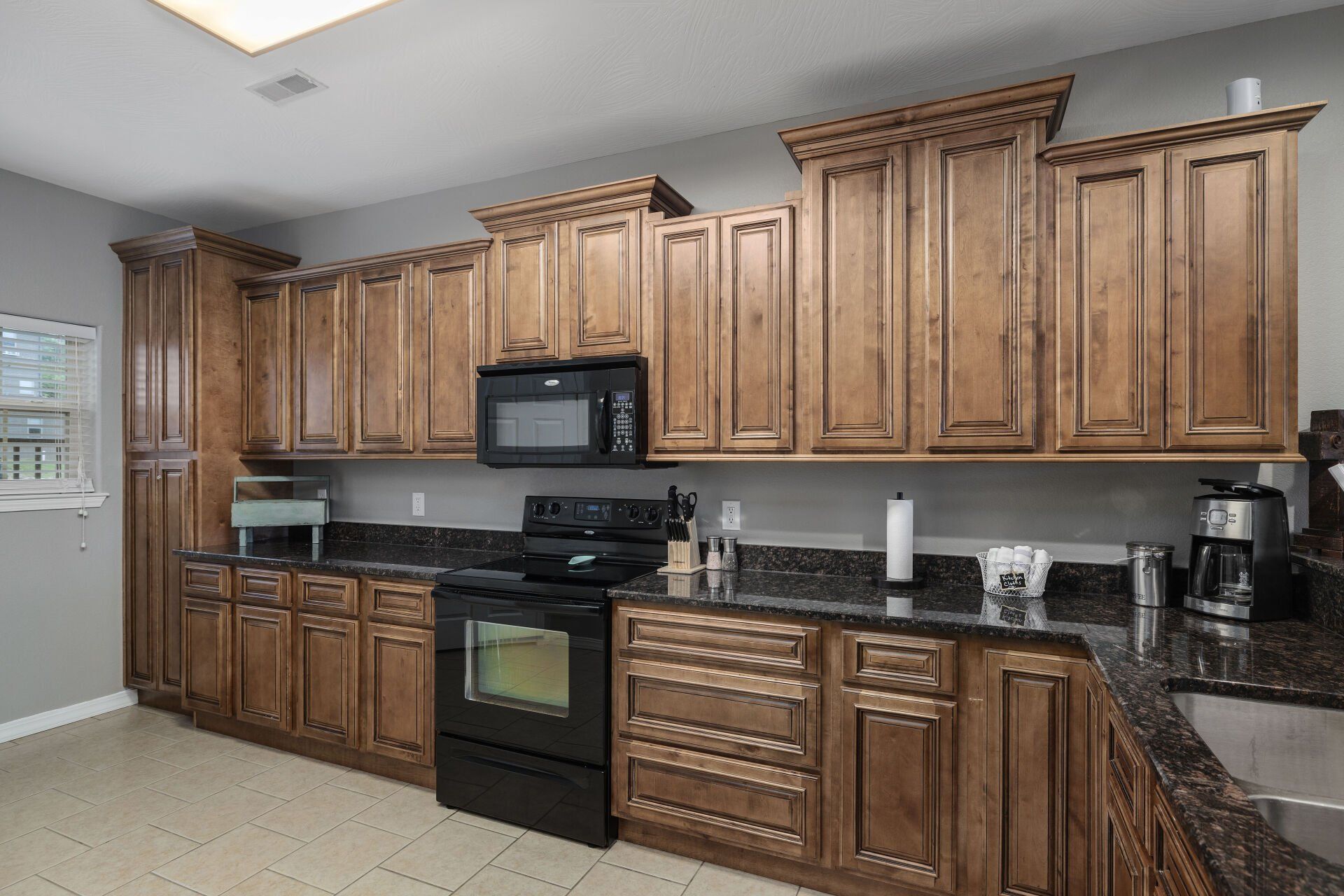 Modern kitchen with wooden cabinets, black countertops, stainless appliances, and beige tile floor