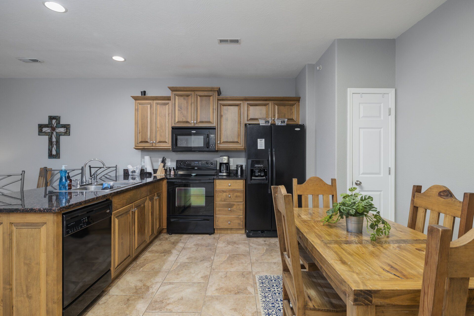 Modern kitchen and dining area with wooden cabinets, black appliances, and a wooden table set for two.