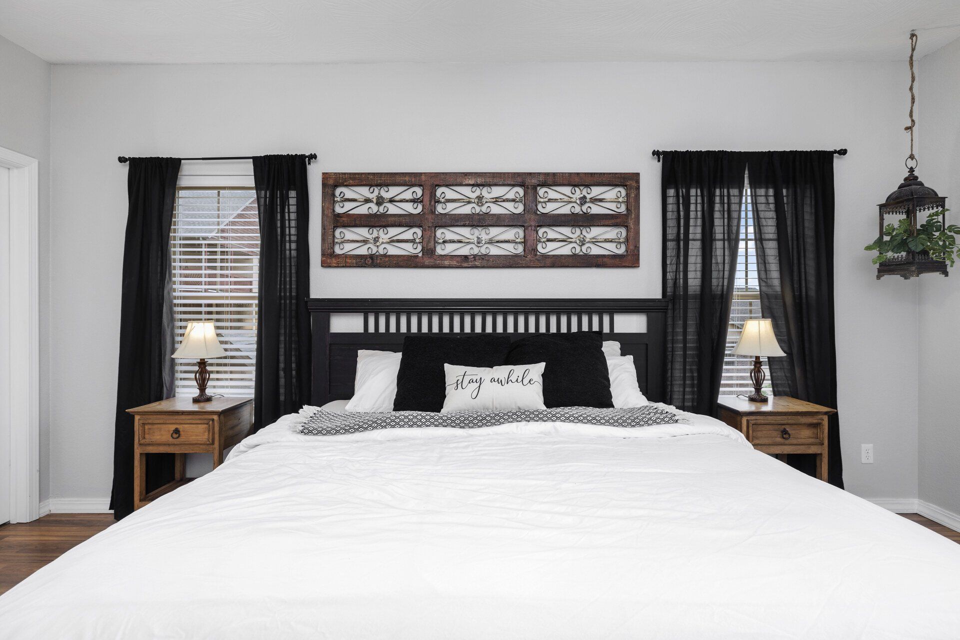 Bright bedroom with a white bed, black curtains, wooden nightstands, and a decorative wall panel above the headboard