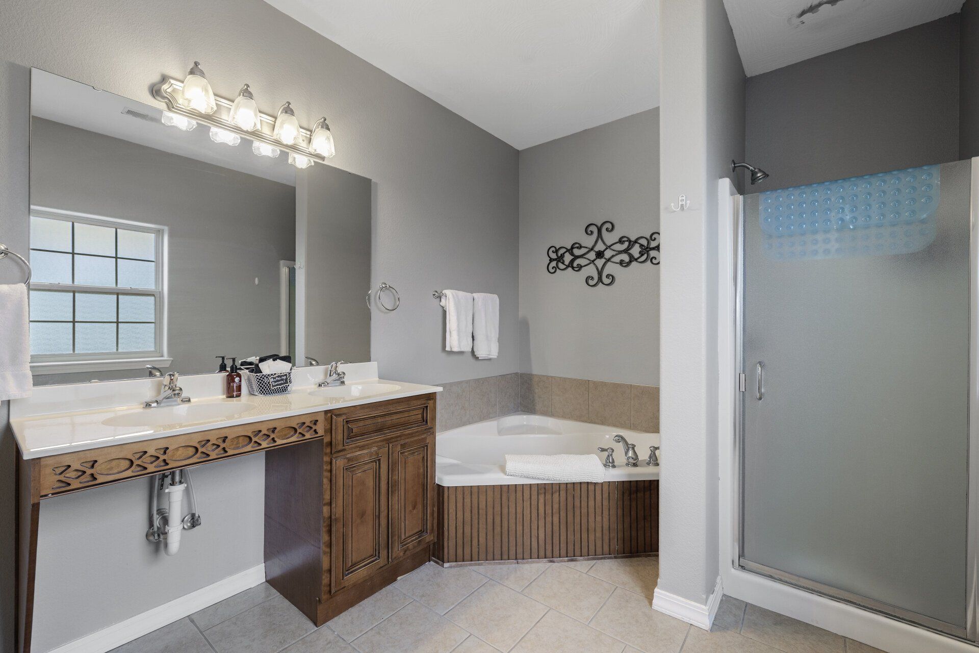 Modern bathroom with vanity, mirror, corner tub, gray walls, and frosted glass shower door