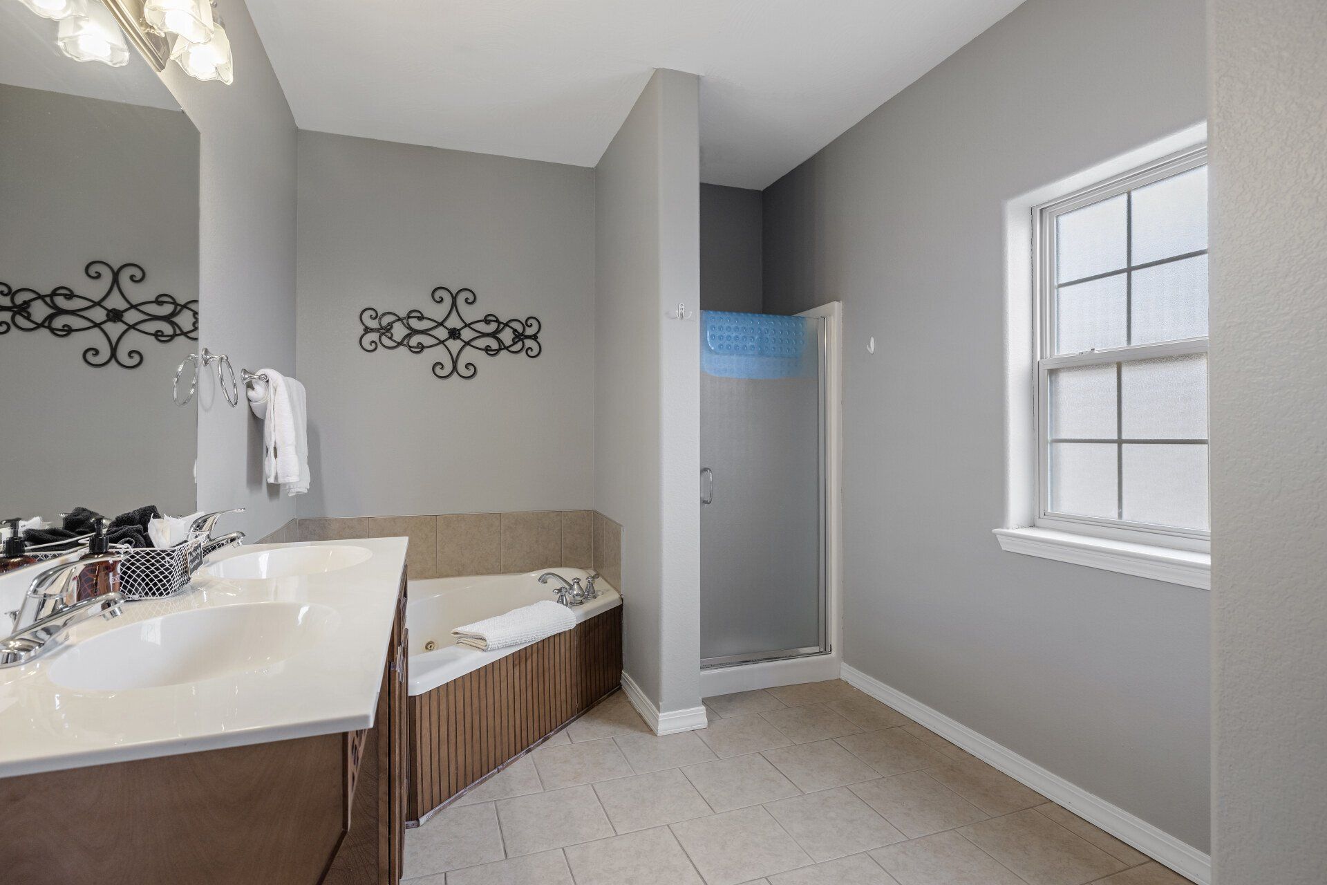 Modern bathroom with double vanity, bathtub, gray walls, and window near a shower area