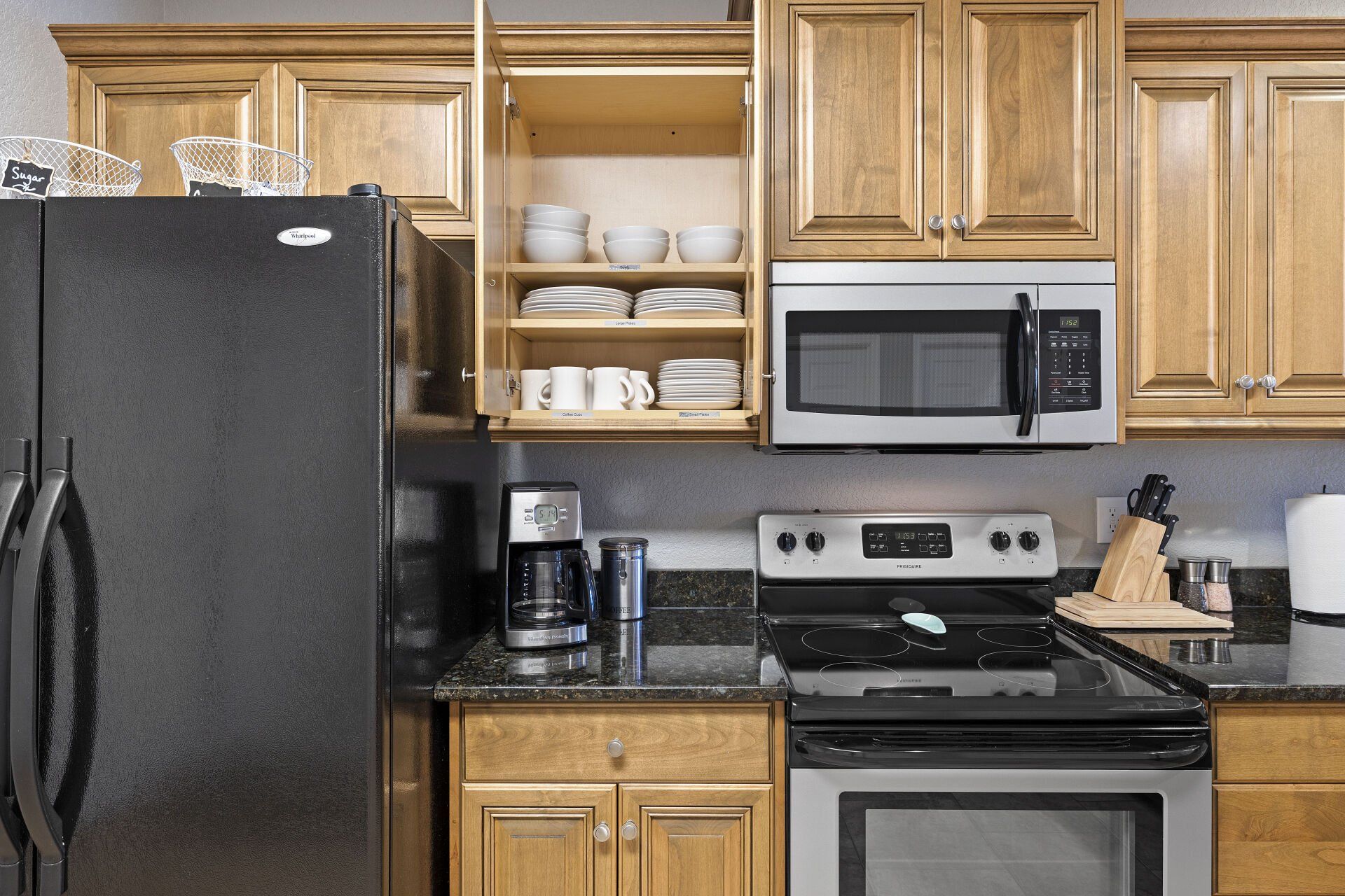 Kitchen with black refrigerator, wooden cabinets, open shelves, microwave, and stove with coffee maker on counter