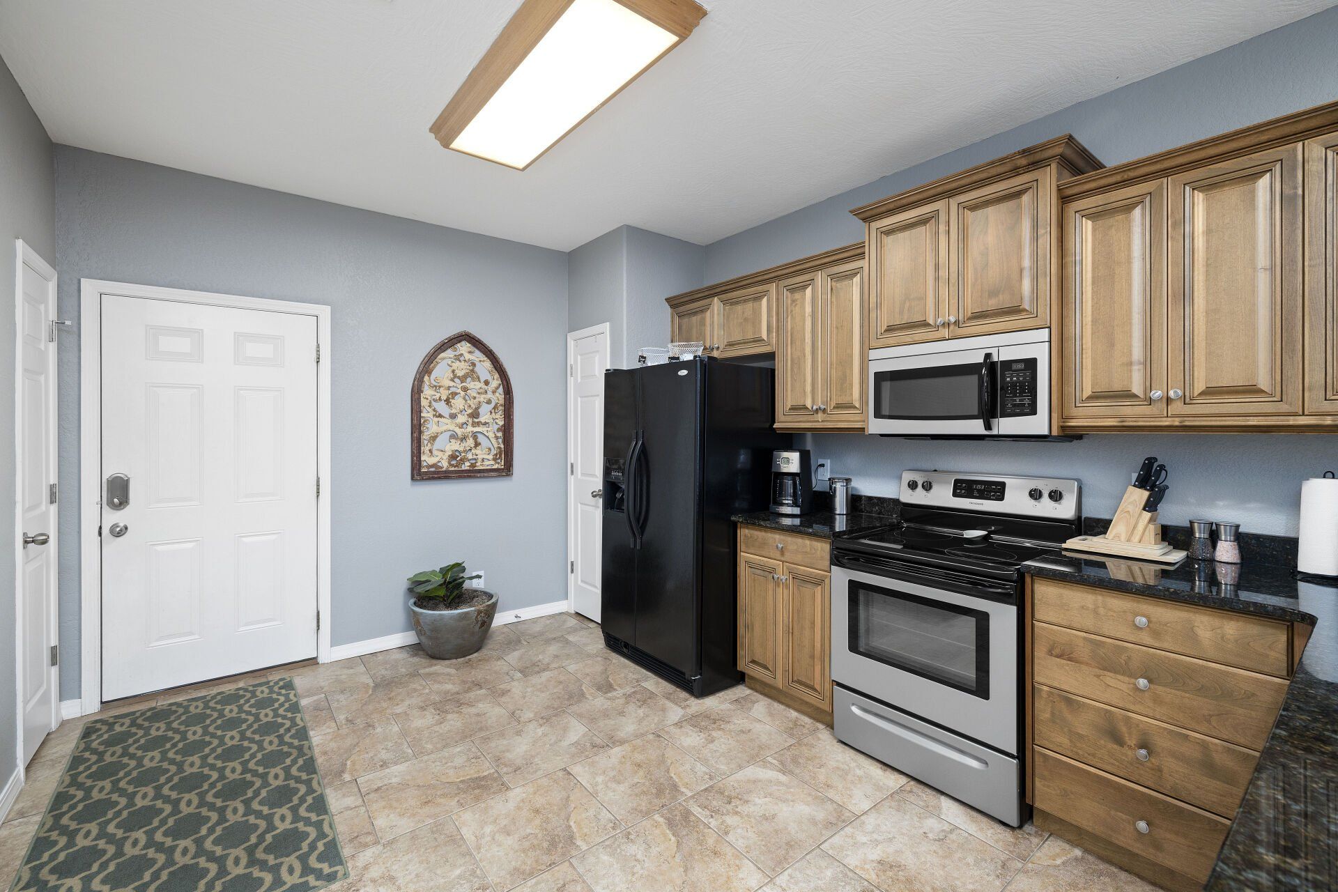 Bright kitchen with wood cabinets, stainless appliances, gray walls, tile floor, and a potted plant by the door