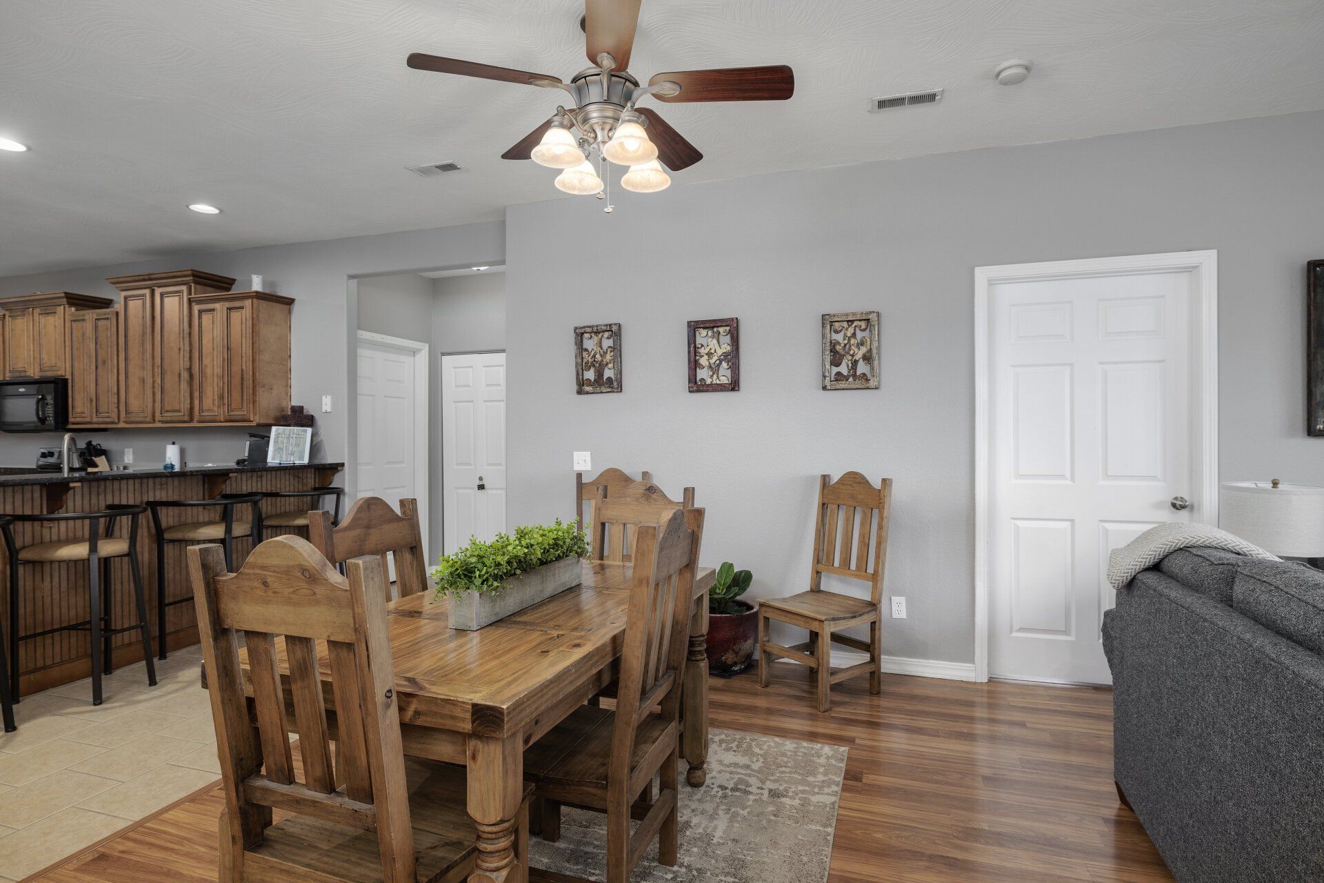 Open-concept dining and kitchen area with wooden table, bar stools, and gray sofa