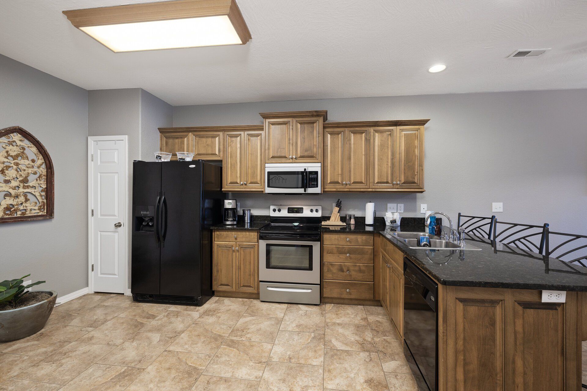 Small kitchen with black appliances, light wood cabinets, tan tile floor, and dark countertop peninsula.