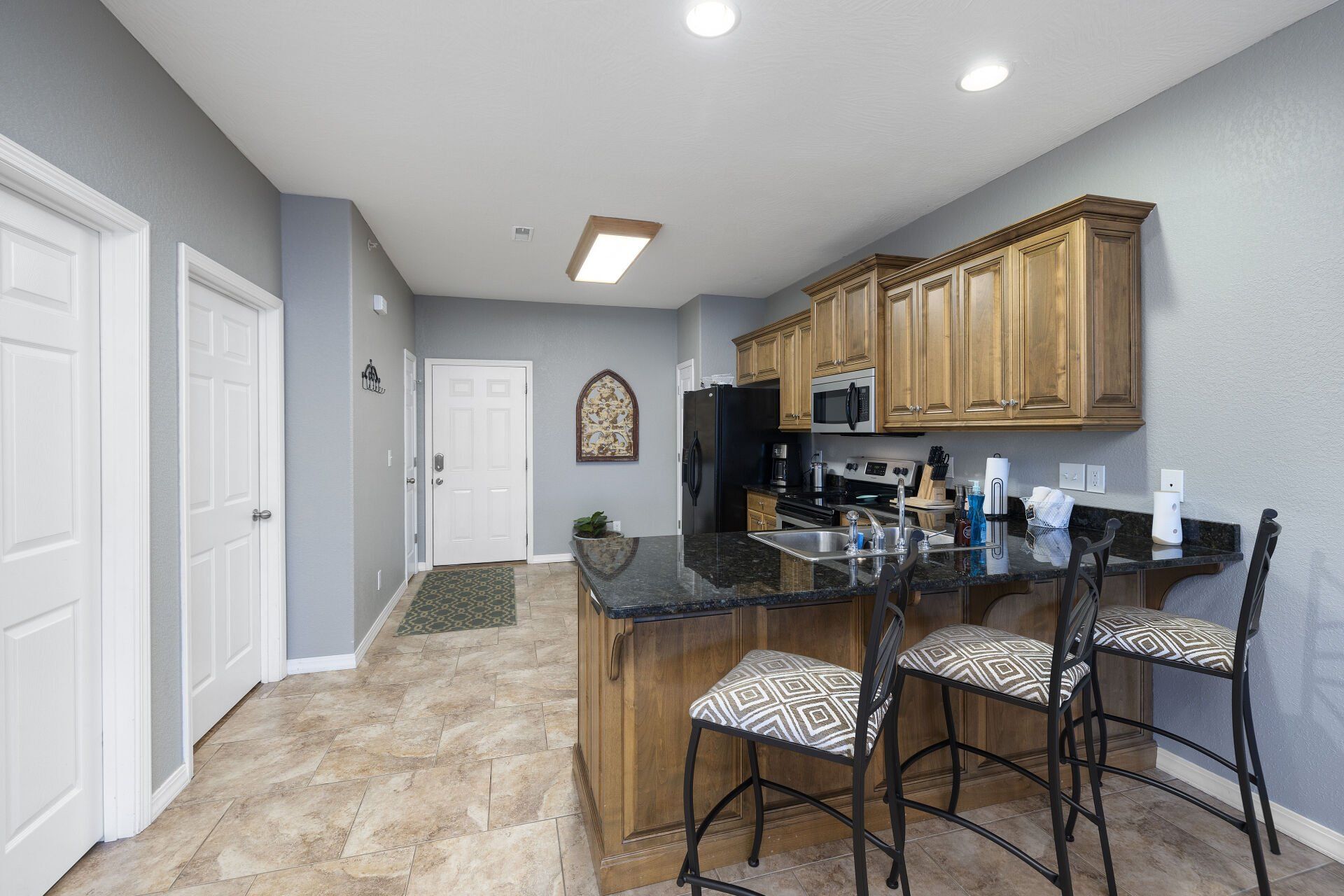 Bright kitchen with wood cabinets, black breakfast bar, and tiled floor in a modern home interior