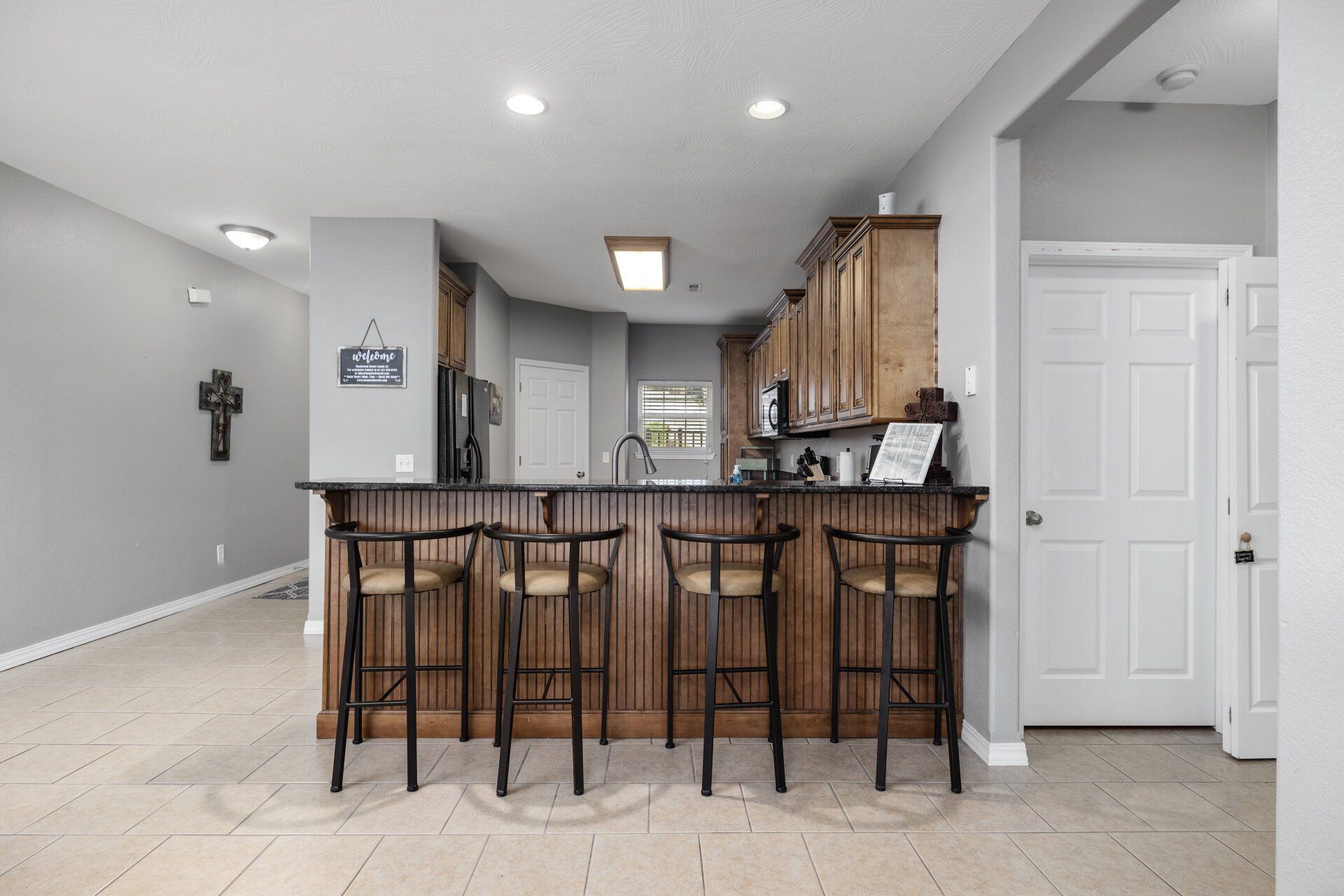 Modern kitchen with a wooden island, barstools, light gray walls, and tile flooring