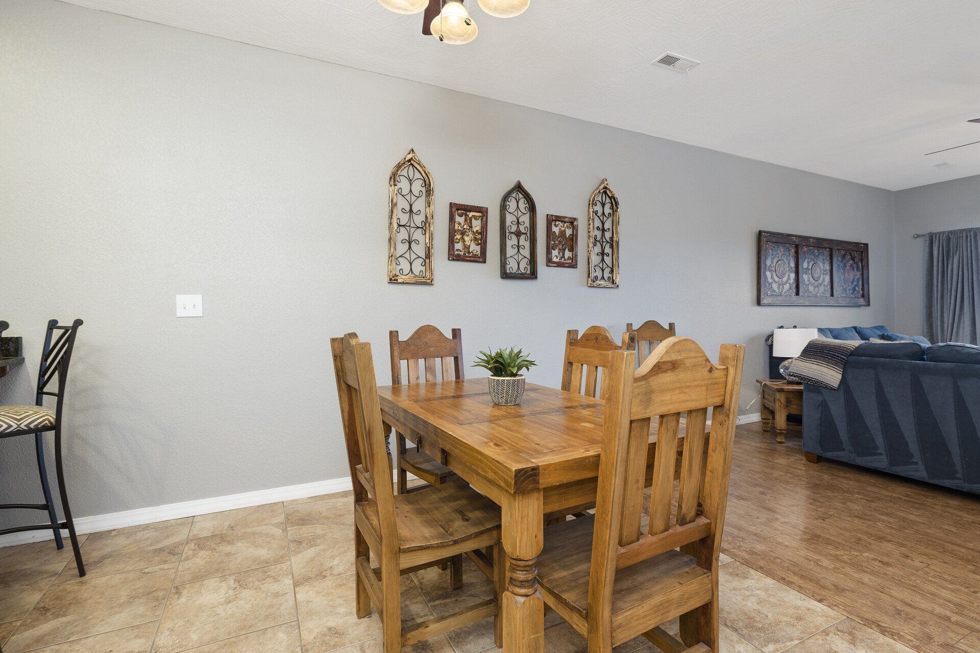 Dining area with wooden table and chairs, gray walls, wall art, and a blue sofa in the background.