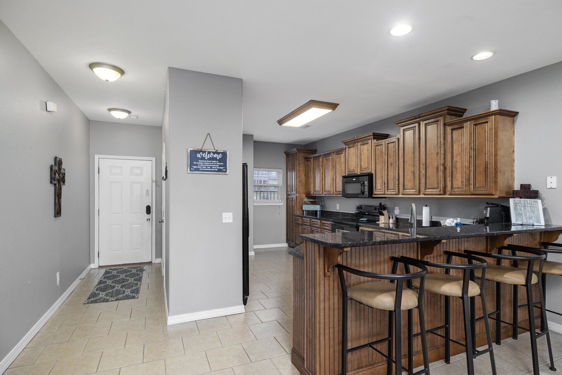 Modern kitchen with wood cabinets, granite island, and breakfast bar beside a hallway and entry door