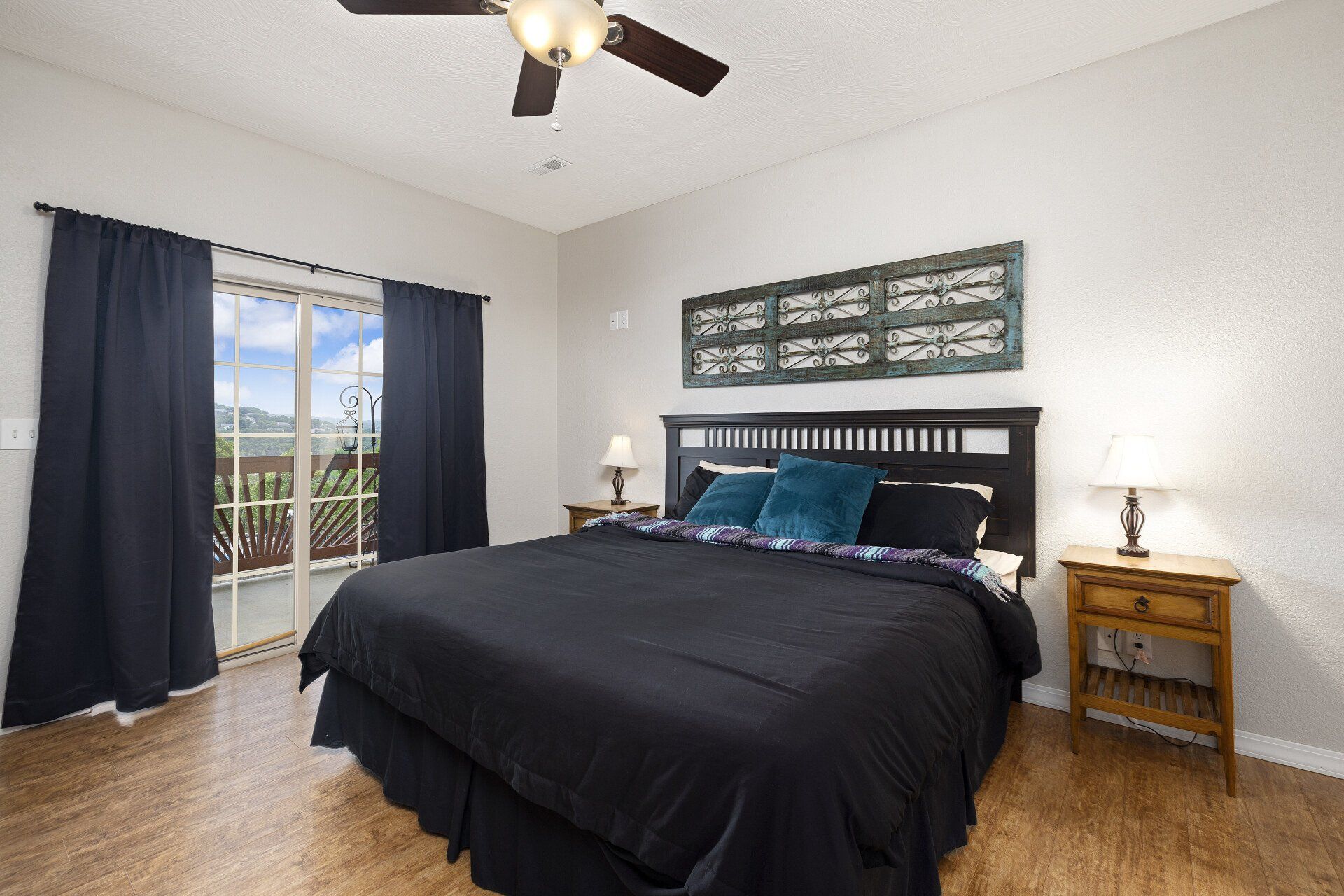 Bedroom with black bedspread, nightstands, lamps, dark curtains, and a balcony door with mountain view.