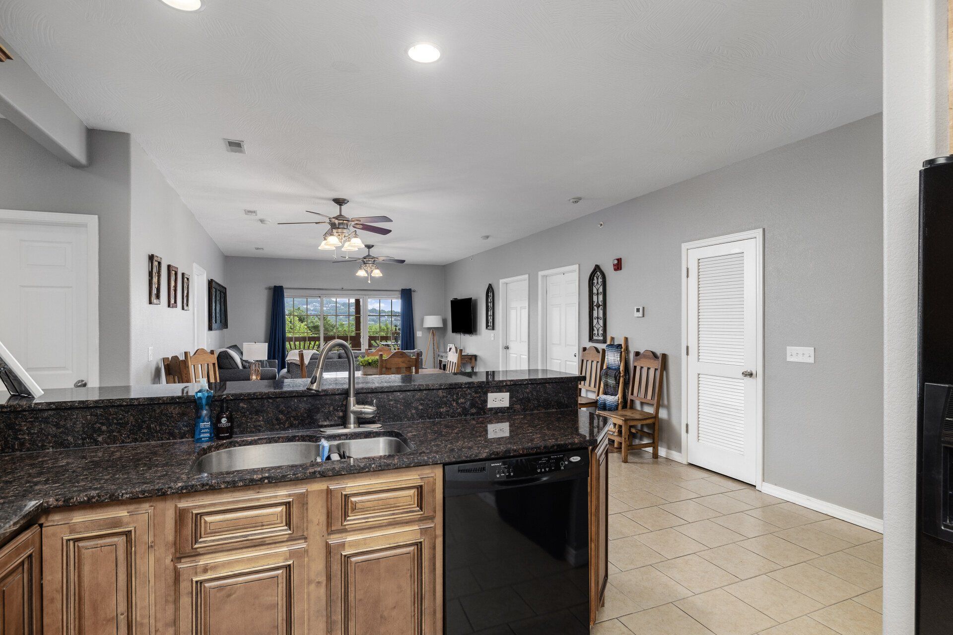 Modern open-concept kitchen with granite island, wood cabinets, tile floor, and view into living room