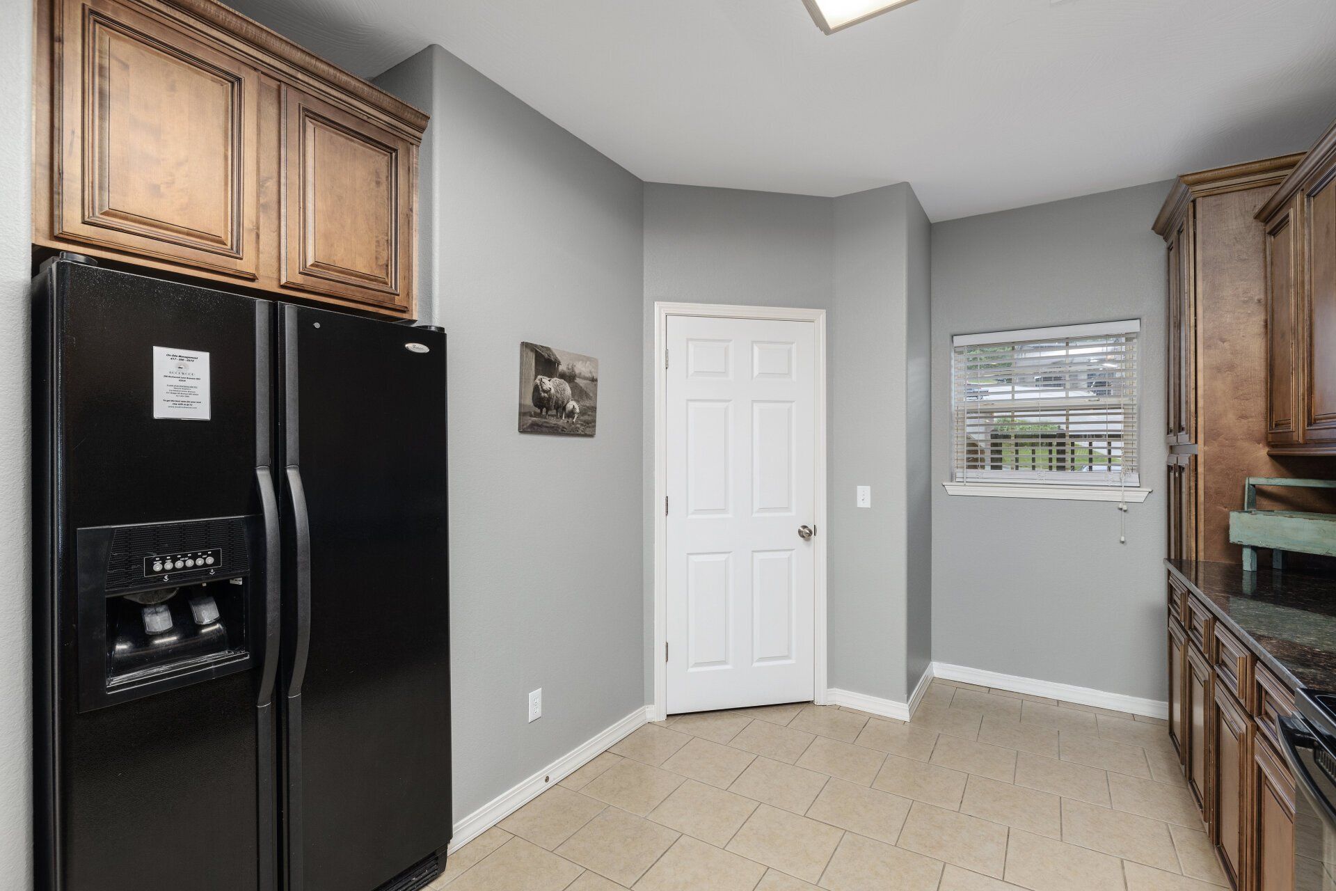 Bright kitchen with black refrigerator, wood cabinets, gray walls, and a white pantry door.