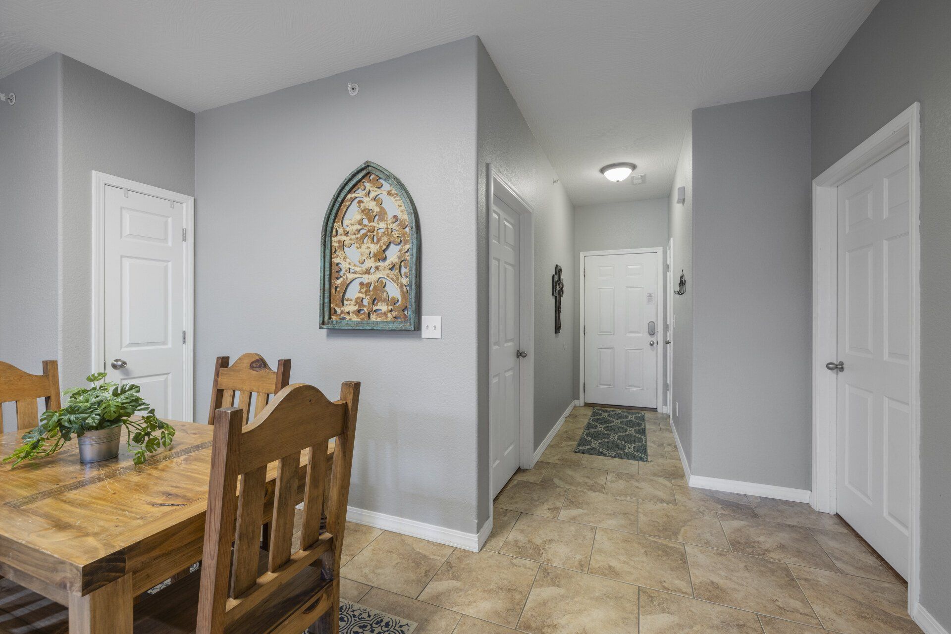 Dining area and hallway in a home with gray walls, tiled floor, white doors, and wall decor