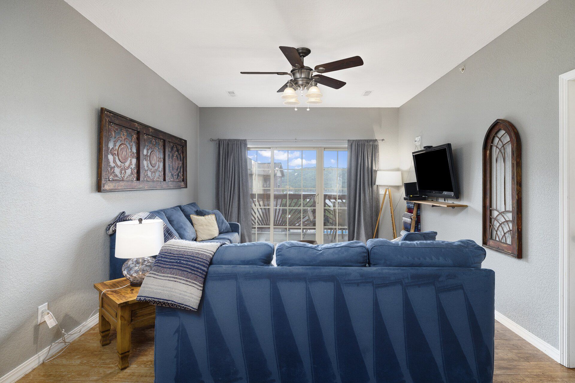 Bright bedroom with blue bedding, gray walls, ceiling fan, and balcony doors with curtains