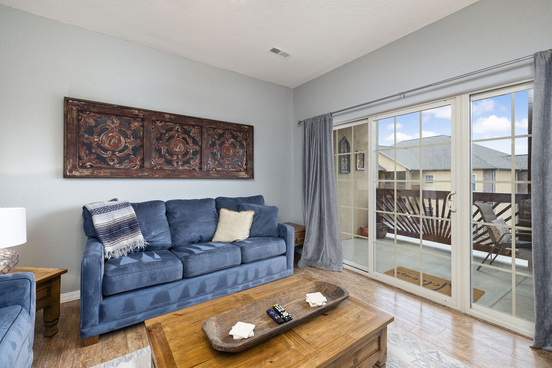 Bright living room with blue sofa, coffee table, wall art, and sliding glass doors to a balcony