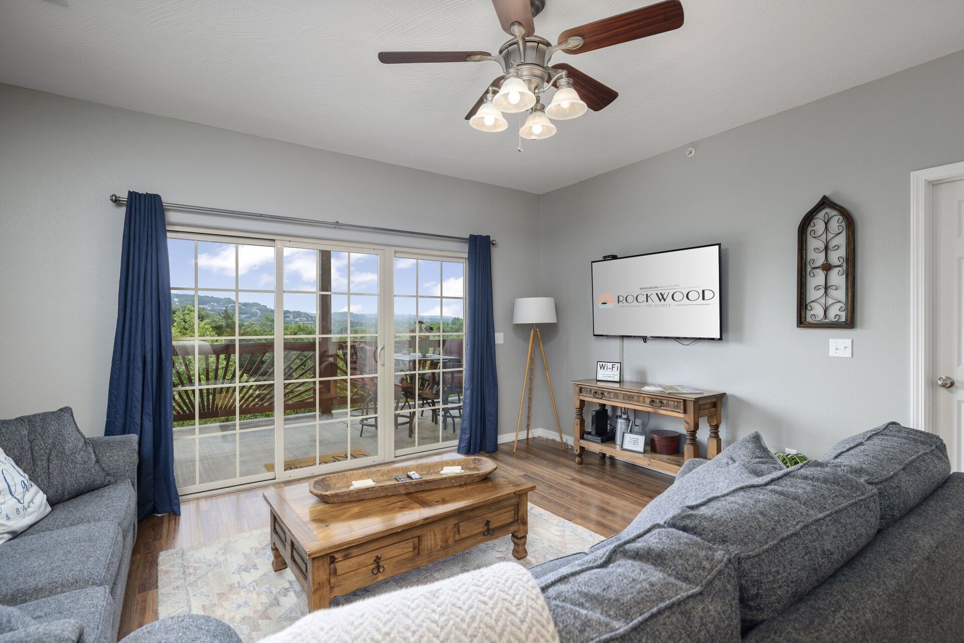 Bright living room with gray sofas, wood coffee table, wall TV, and sliding glass doors to a balcony.