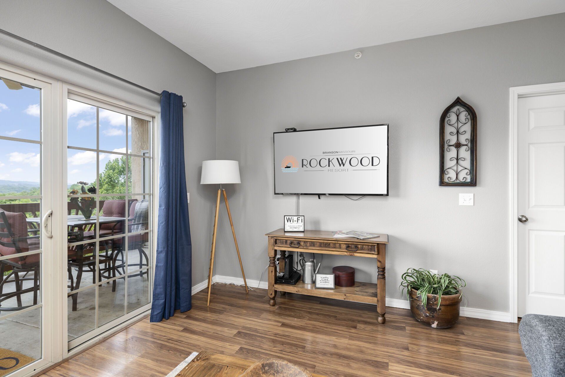 Bright living room with sliding glass doors, blue curtains, wood floors, and a console table with decor.