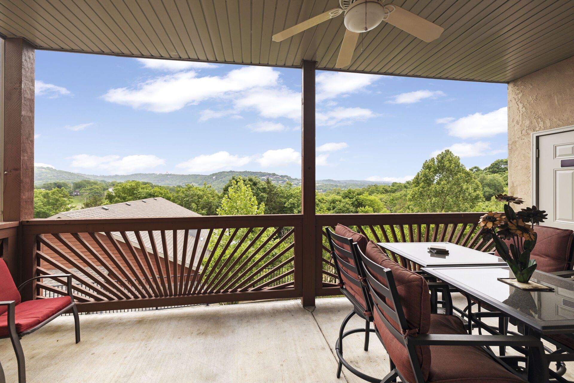 Covered balcony with patio table and chairs overlooking a green landscape and distant hills
