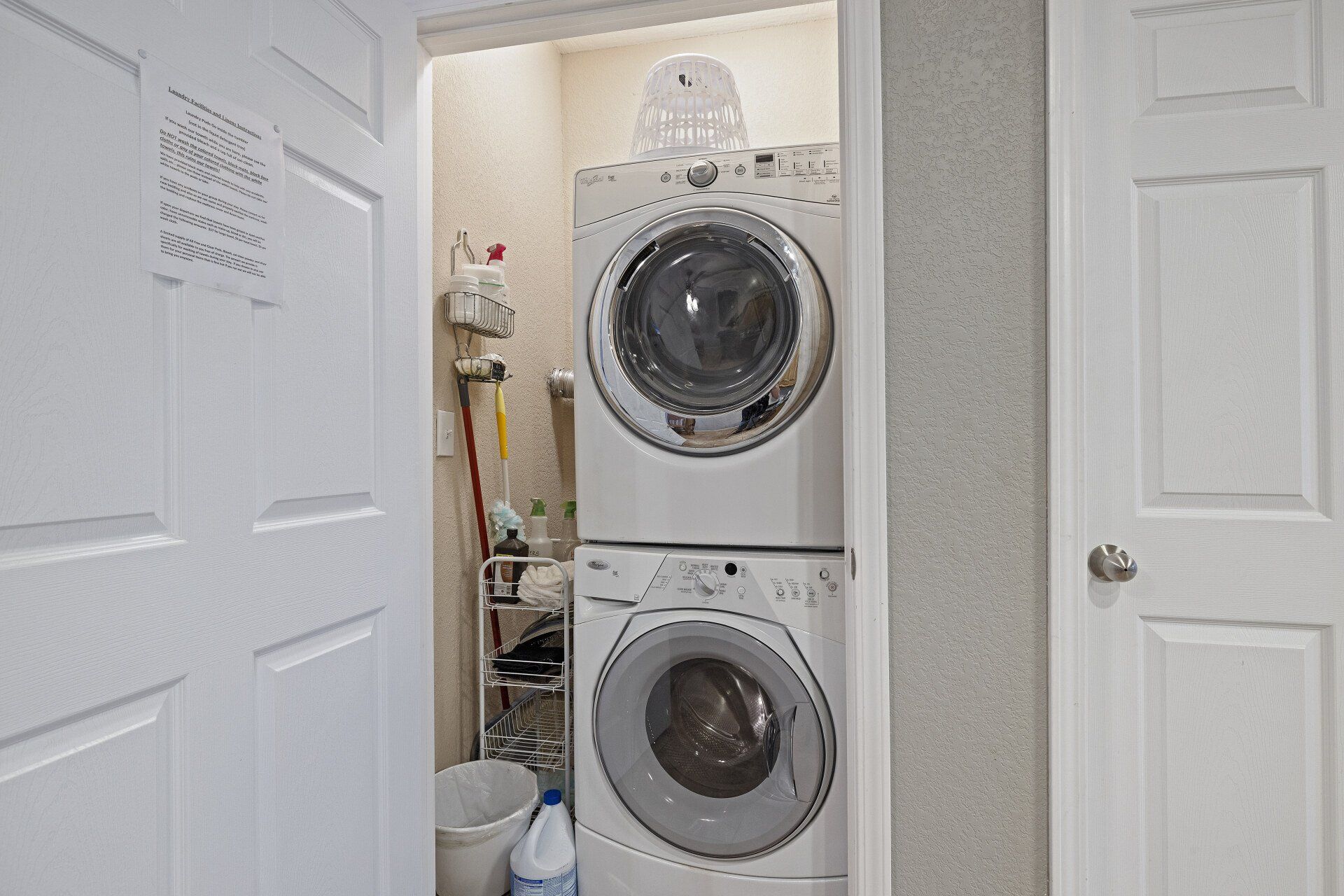 Stacked washer and dryer in a small laundry closet with white doors open