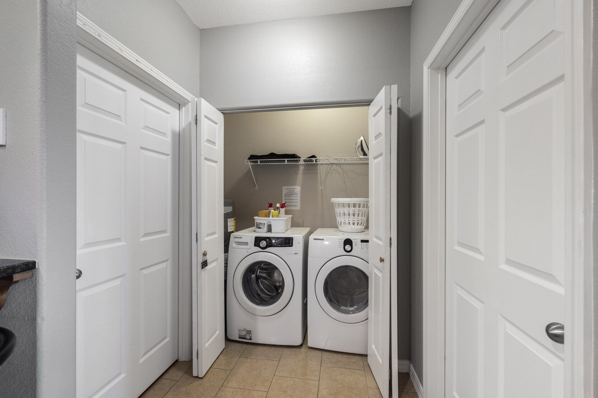 Laundry room with white washer and dryer in a narrow hallway, doors open on both sides.