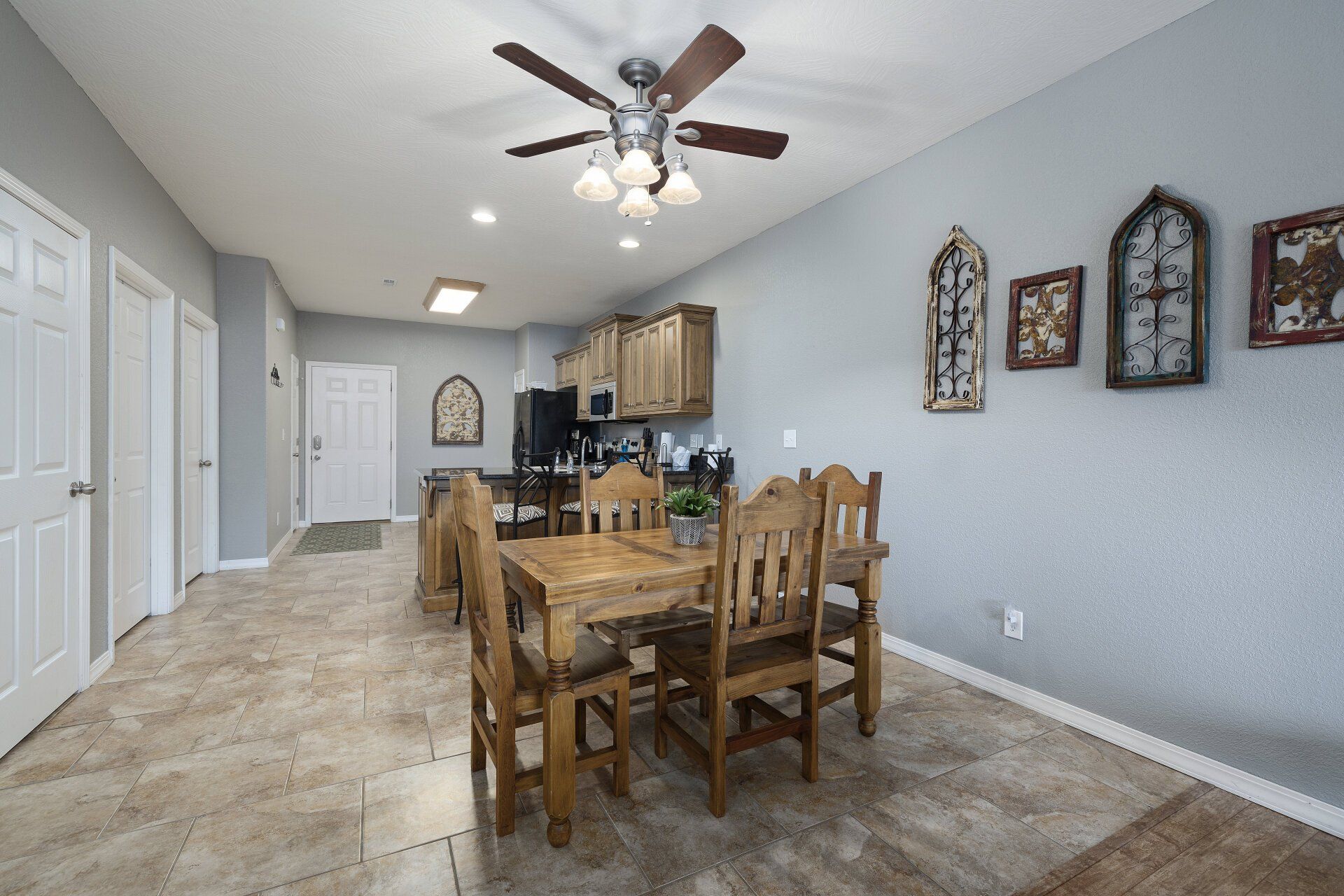 Dining area with wooden table and chairs, ceiling fan, and kitchen in a light blue open-plan room