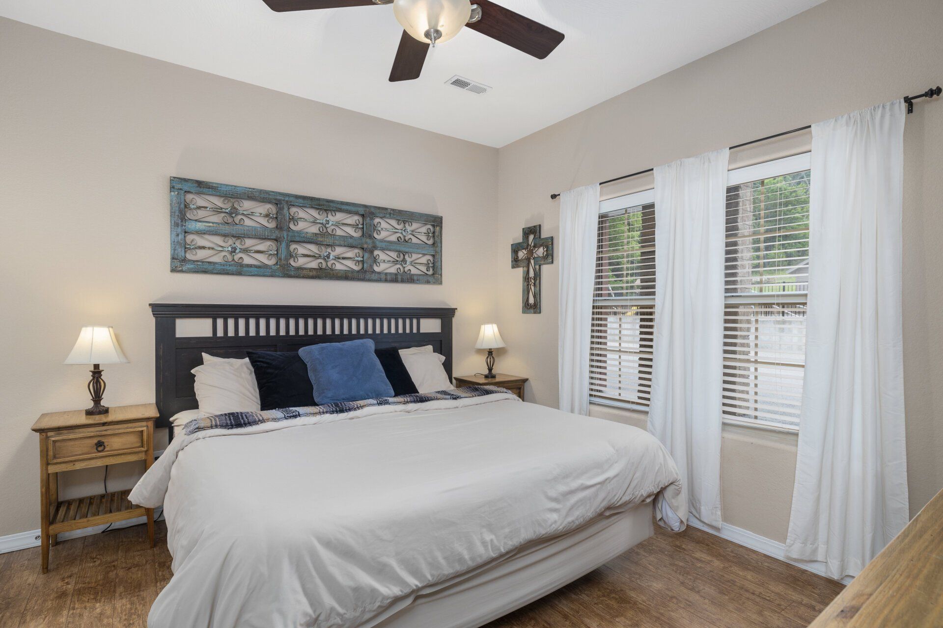 Bright bedroom with a dark wood bed, white bedding, bedside lamps, and large windows with curtains