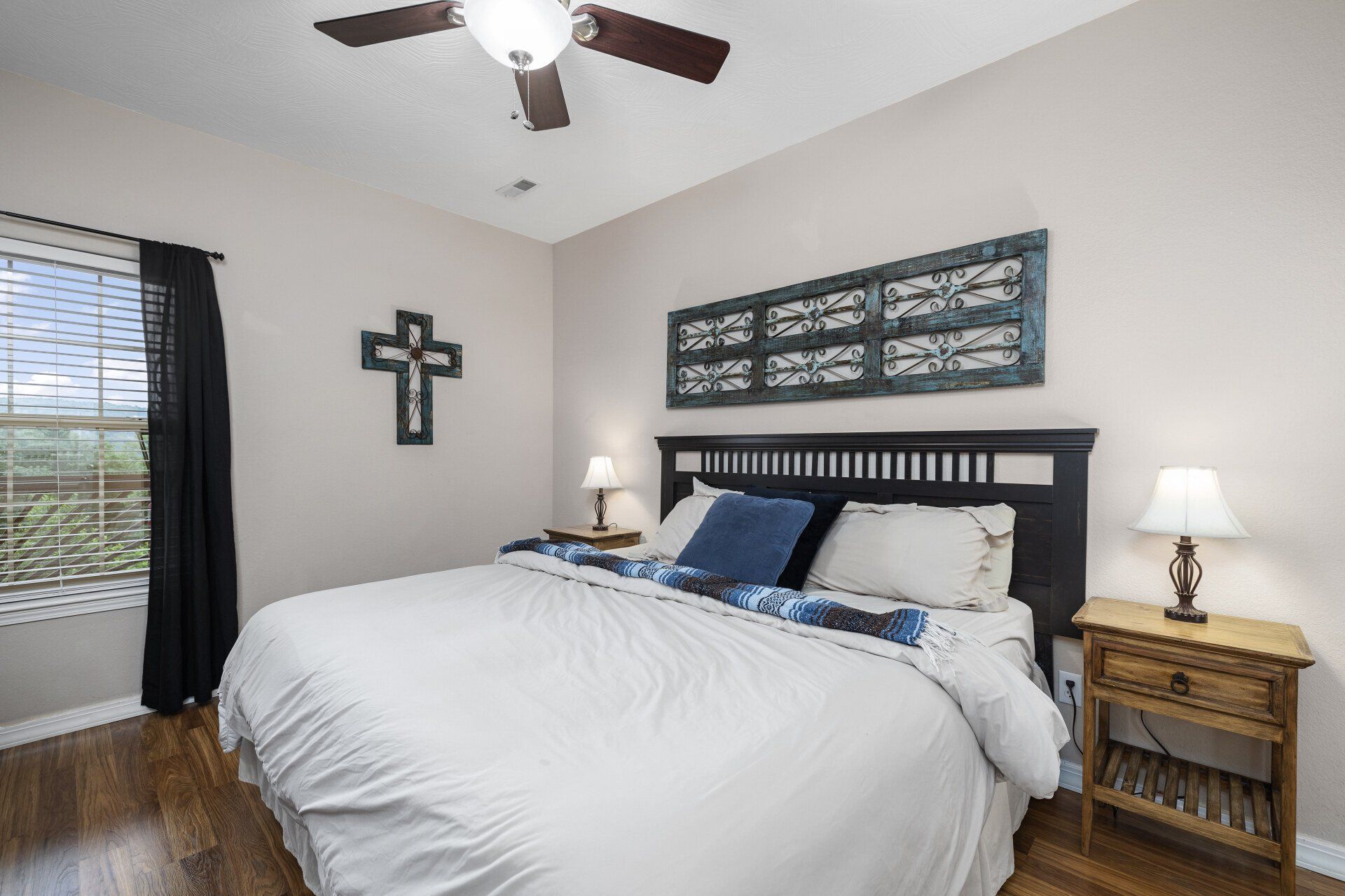 Bright bedroom with a large bed, dark wood furniture, wall decor, and a ceiling fan.