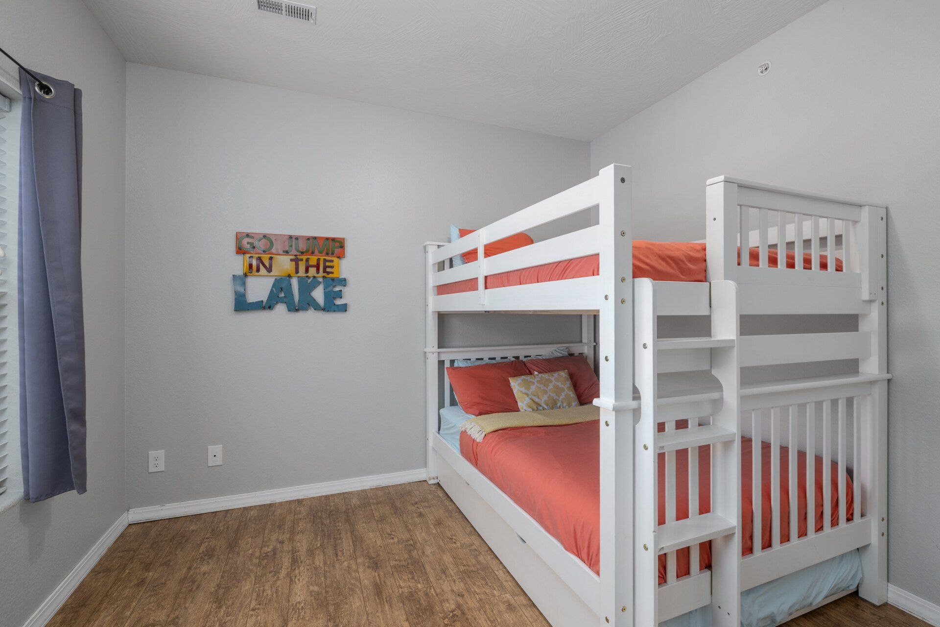 Child’s bedroom with white bunk beds, orange bedding, gray walls, and a “Lake” wall sign